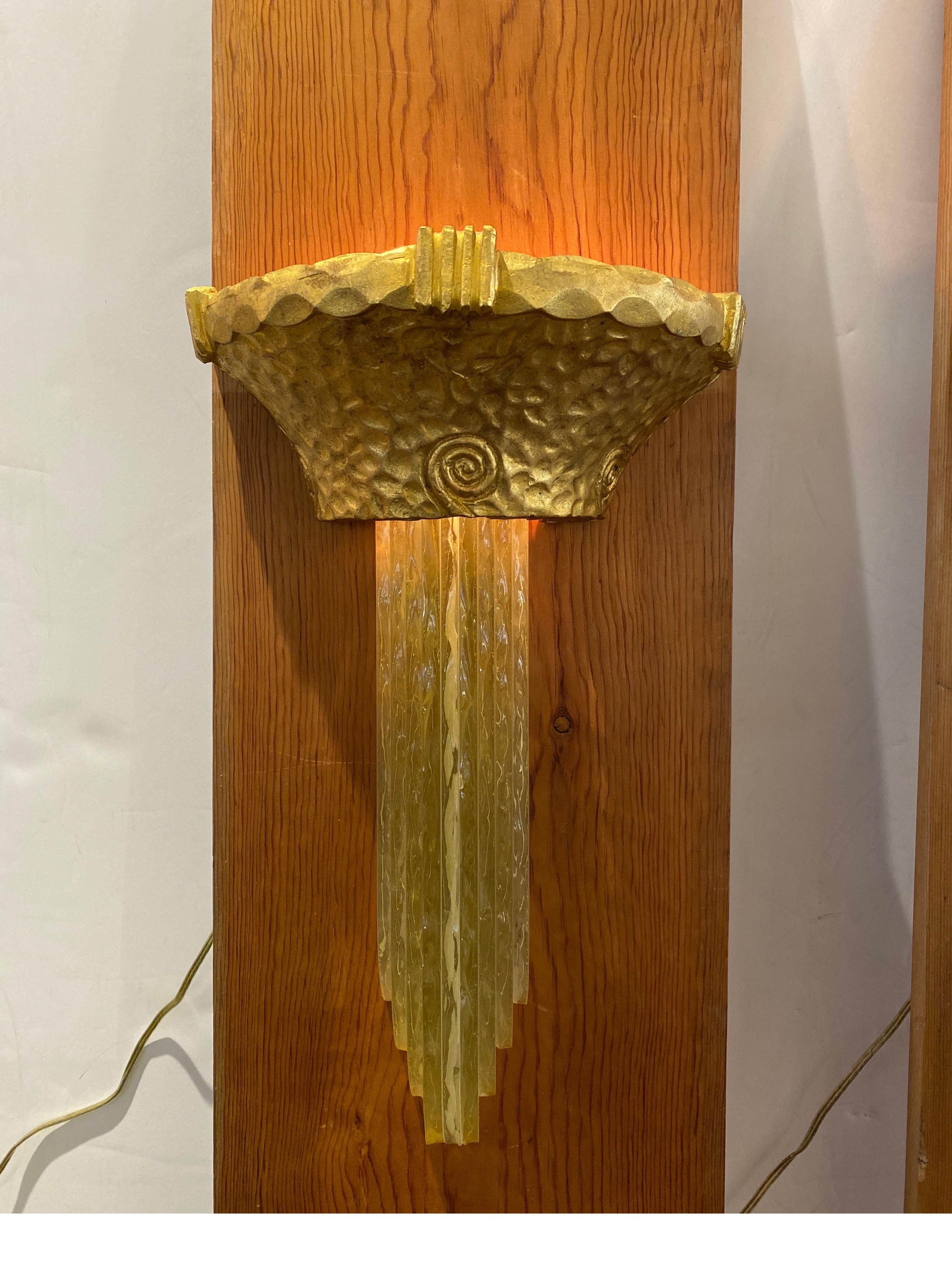 Remarkable pair of hammered bronze and stacked glass Art Deco wall sconces. The hammered gilt bronze surface with art deco decorations with variegated stacked glass panels that fit into the cast bronze tops and diffuse the light. Each one takes two