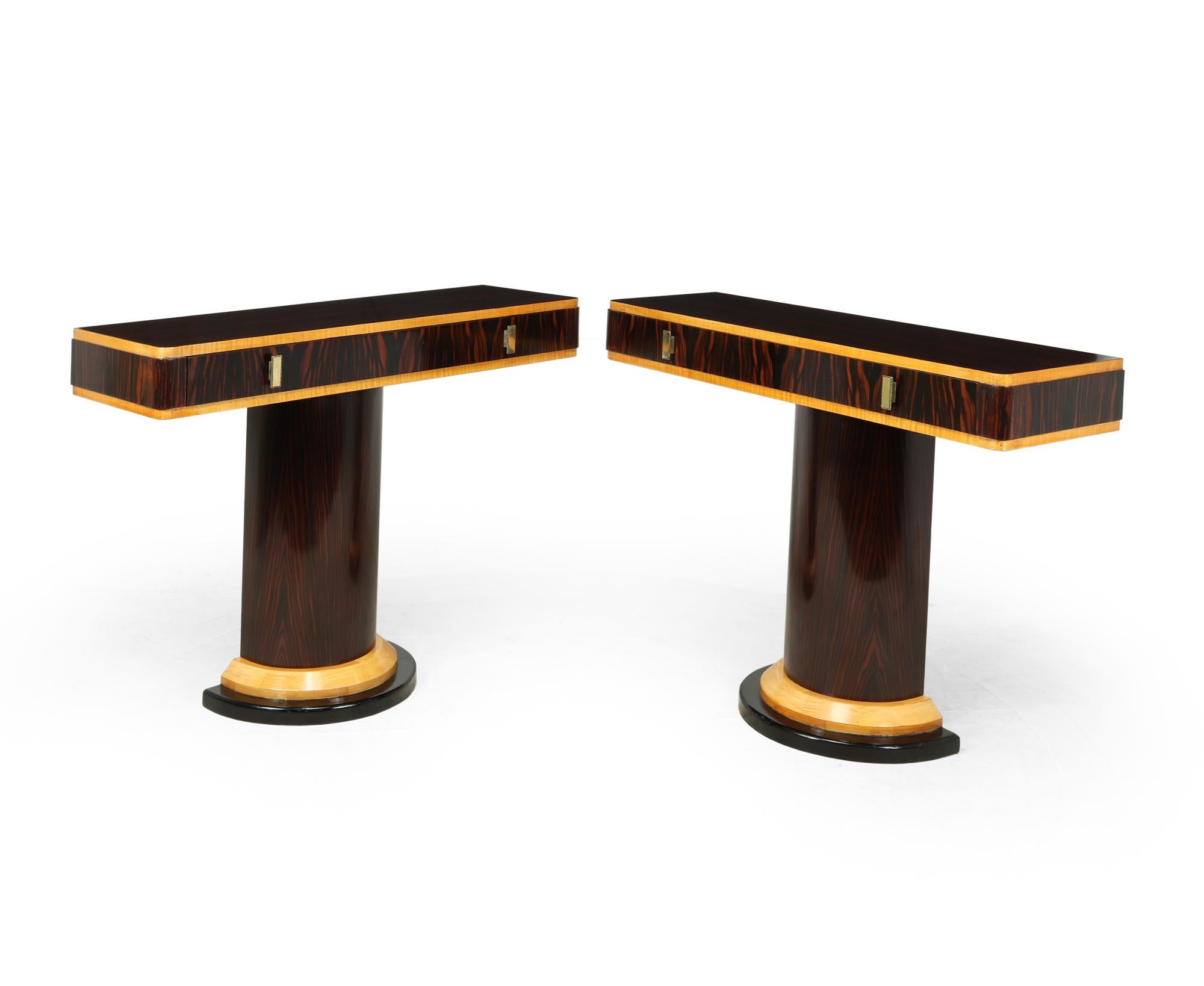 A pair of entrance hall console tables produced in France in the 1920’s, oak and mahogany with luxurious Macassar ebony veneers with sycamore banding. The top has a single long drawer and stands on a demi-lune column with heavier stepped plinth.