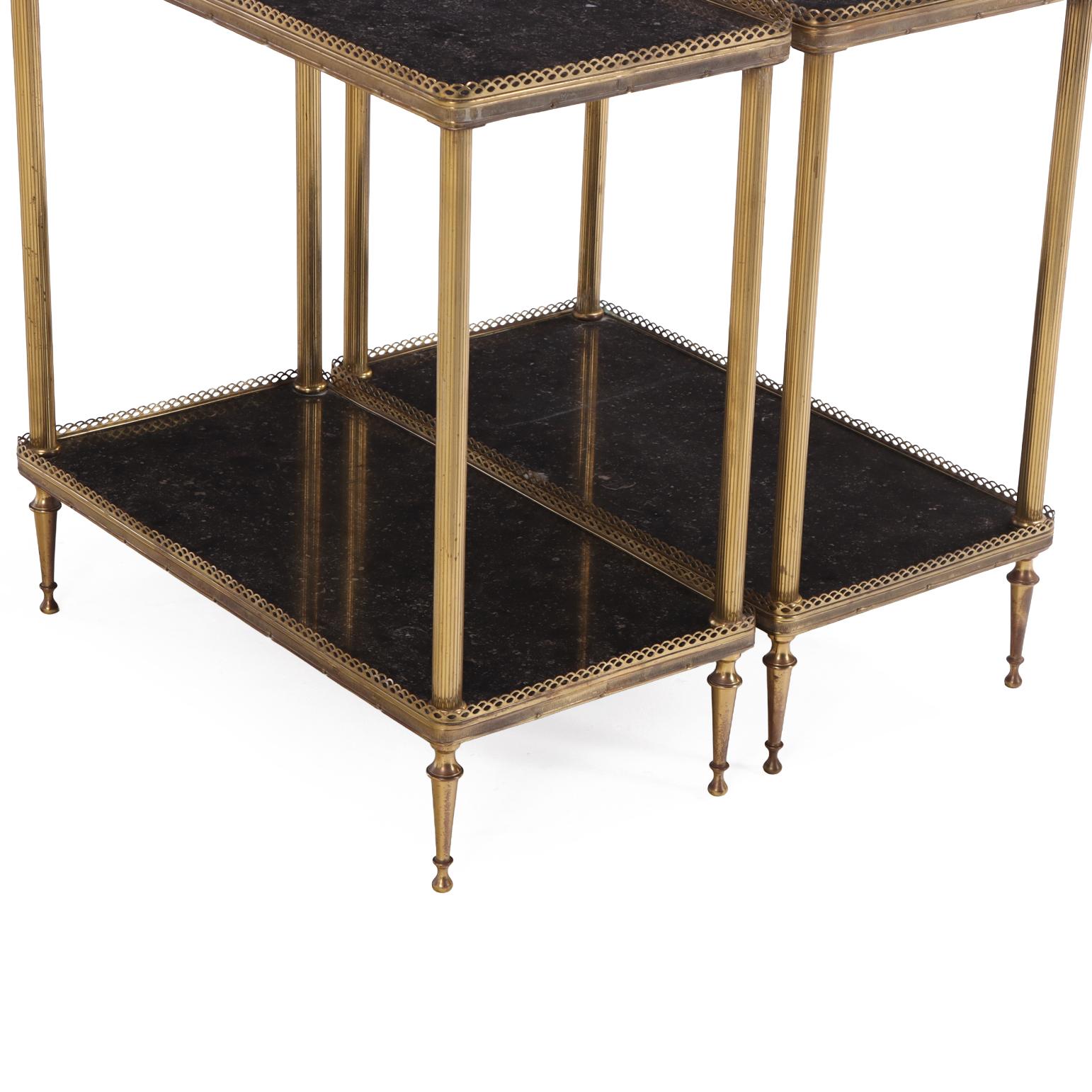 Elegant pair of mid-century French brass tables, each composed of two tiers fitted with black marble shelves. The brass galleried edges frame the stone beautifully, adding both function and refinement. Supported by fluted brass legs terminating in