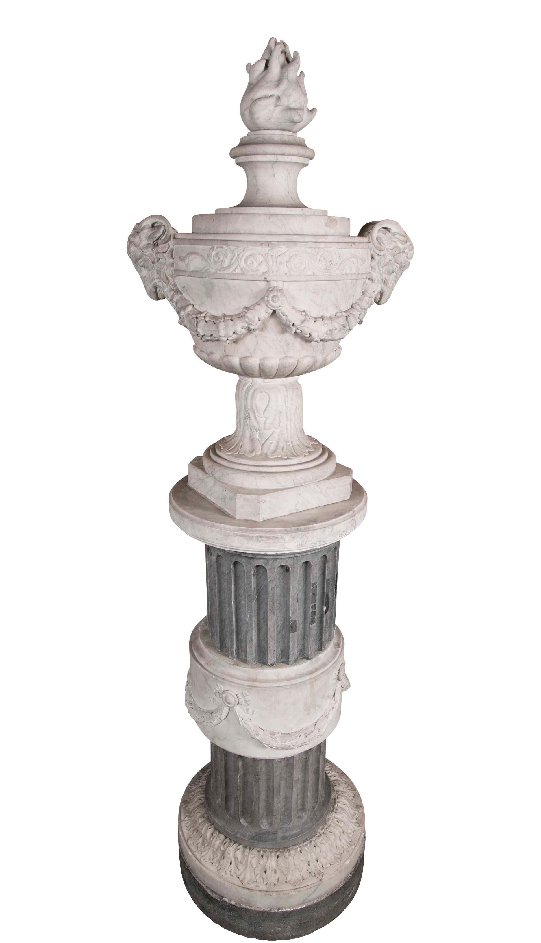 A pair of carved neoclassical marble urns each with flambeaux finial and double ram's head handles with garland.
 