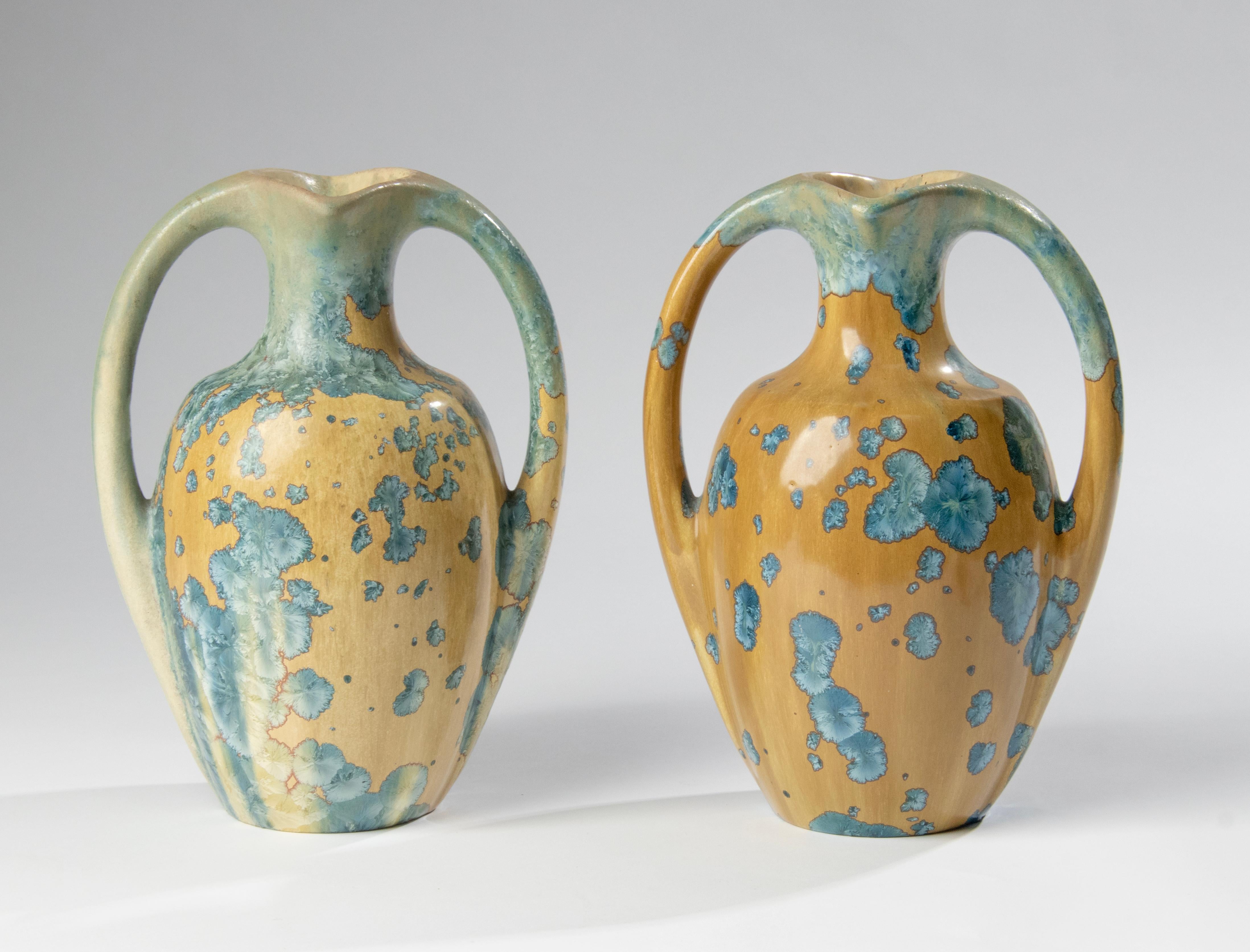 A nice pair of two ceramic Art Deco vases from La Faïencerie Héraldique de Pierrefonds Pottery of France. The vases are designed with two curved handles and decorated in a golden brown glaze with bright blue crystalline clusters scattered around the