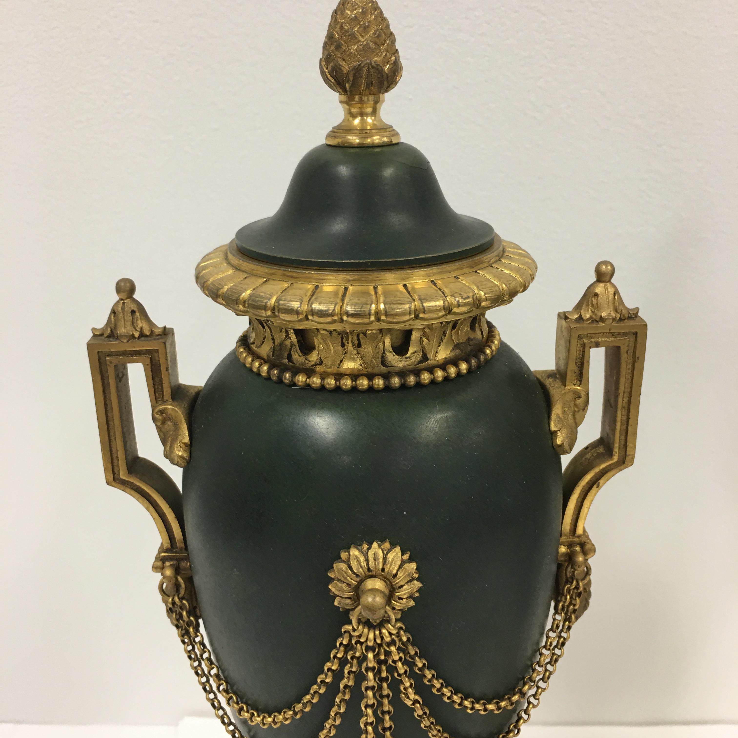 A superb pair of French Empire period painted bronze and ormolu casolettes. Each vase is raised by a fluted socle shaped ormolu pedestal. The urn shaped painted green body is decorated with ormolu draped chains terminated with finely chased tassels