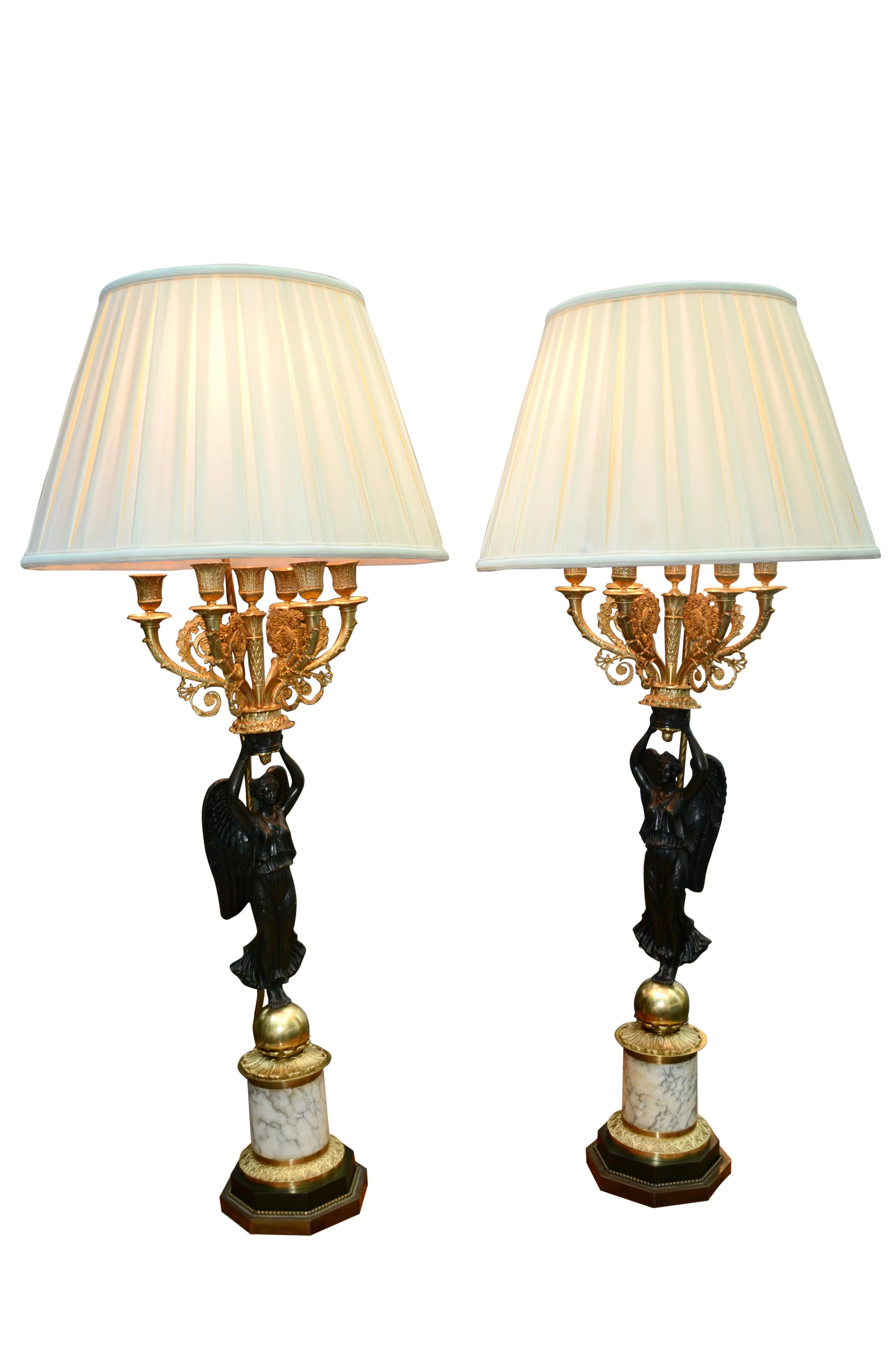 A fine pair of late 19thC French Empire style candelabra now wired into lamps. The very well cast and patinated winged Victory or Nike stands on a gilded ball on a further circular mottled white marble base, the top and bottom with gilded trim. The