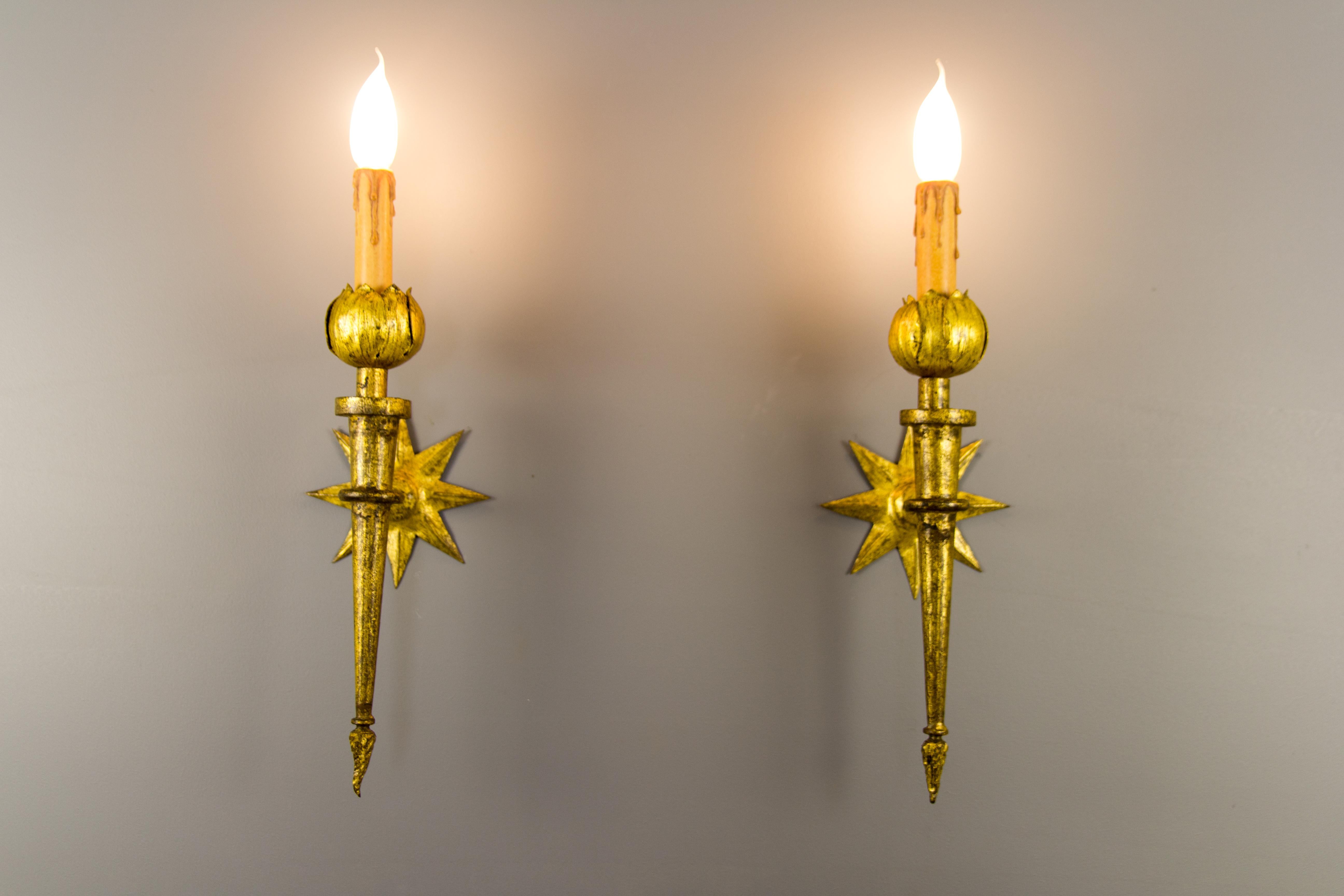 Superb pair of gold patinated wrought iron wall sconces after Gilbert Poillerat. Sockets are surmounted with petals and adorned at the base with stylized flames. These beautiful sconces have star-shaped wall mount. Each sconce is newly rewired and