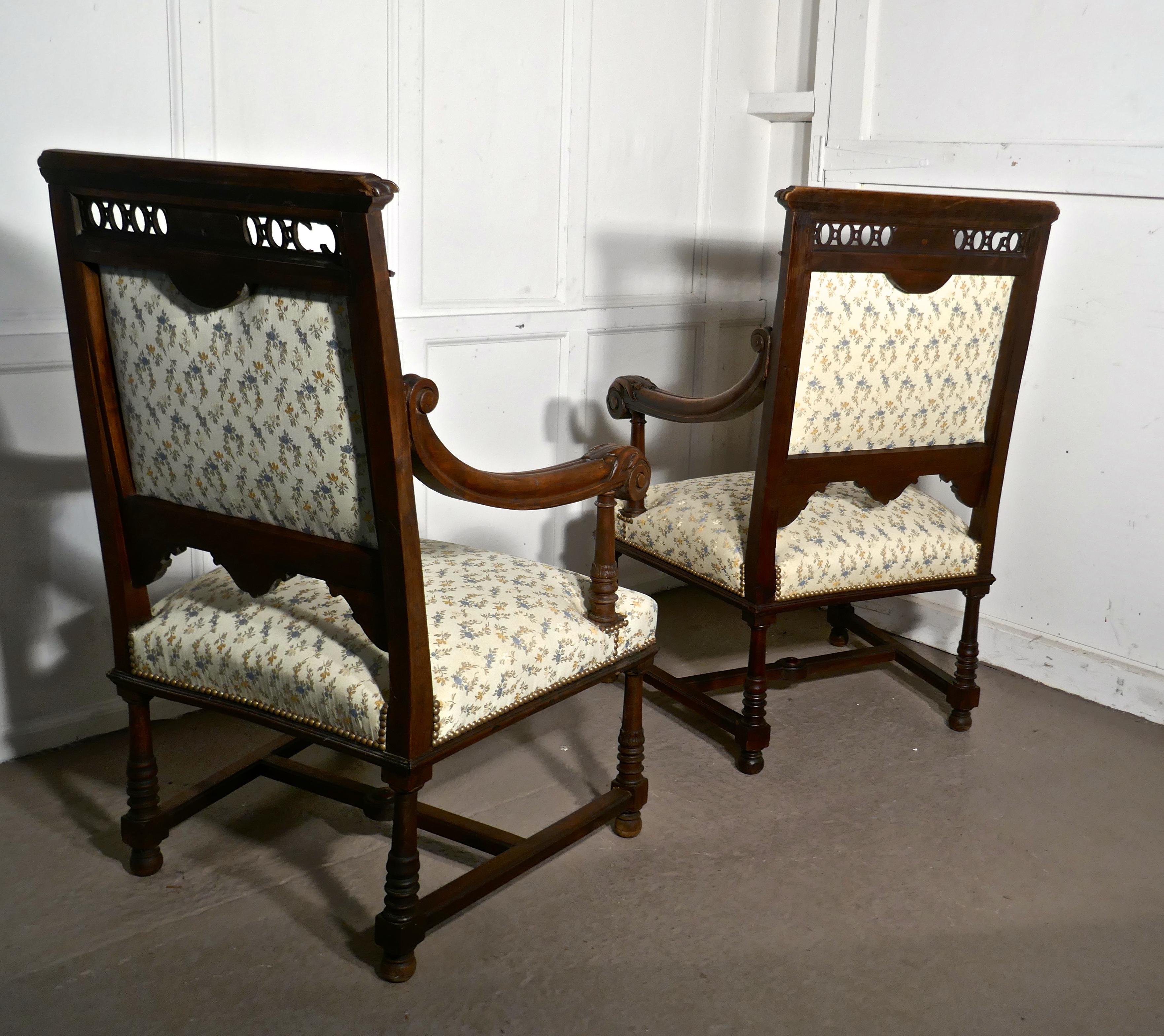 A pair of French Gothic walnut library throne chairs 

These beautiful wide carved chairs each have a different carved face in the back rail, acanthus leaf carved arm rests and a sturdy H stretcher at the floor

They have attractive silk