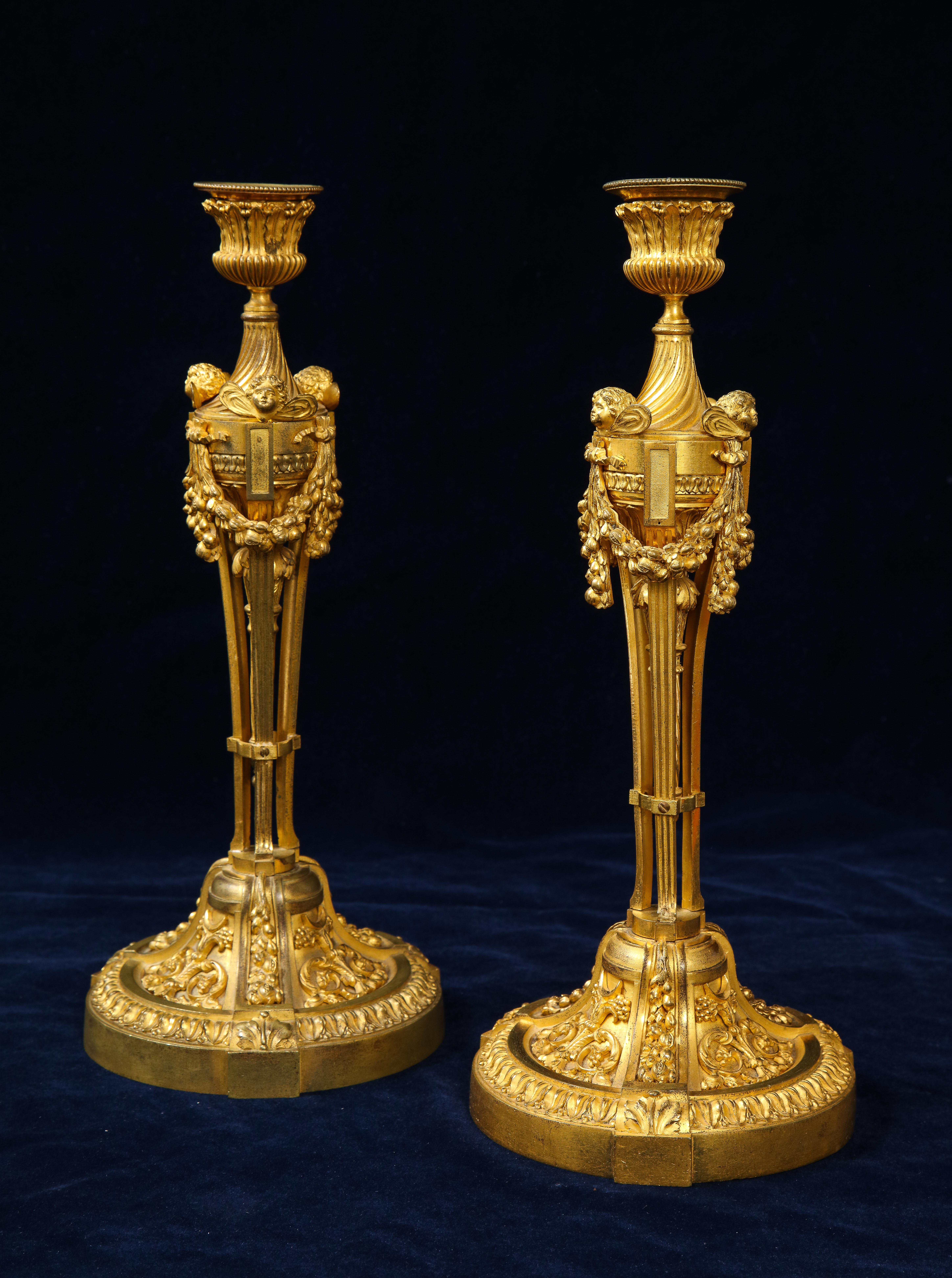 A spectacular pair of French Louis XVI ormolu candlesticks with Putti Masks and Garlands. The socket is very intricately sculpted with beading, acanthus leaves, and fluted bottom. Beneath the socket and down a swirling fluted neck, three putti masks