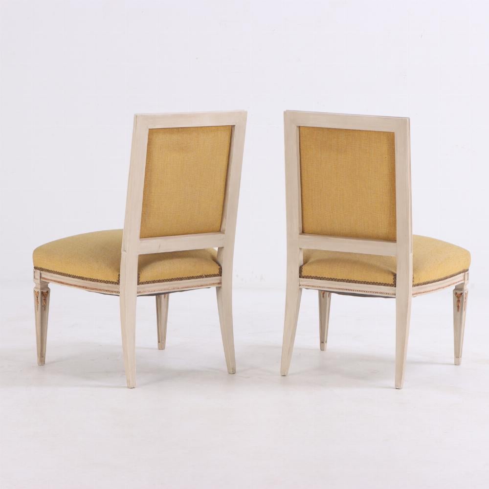 These striking painted and giltwood chairs have straight crests, rectangular backs, and seats supported by by four slender, square tapering legs with blocked corners and gilt foliate embellishments. The seat and back support are upholstered in a