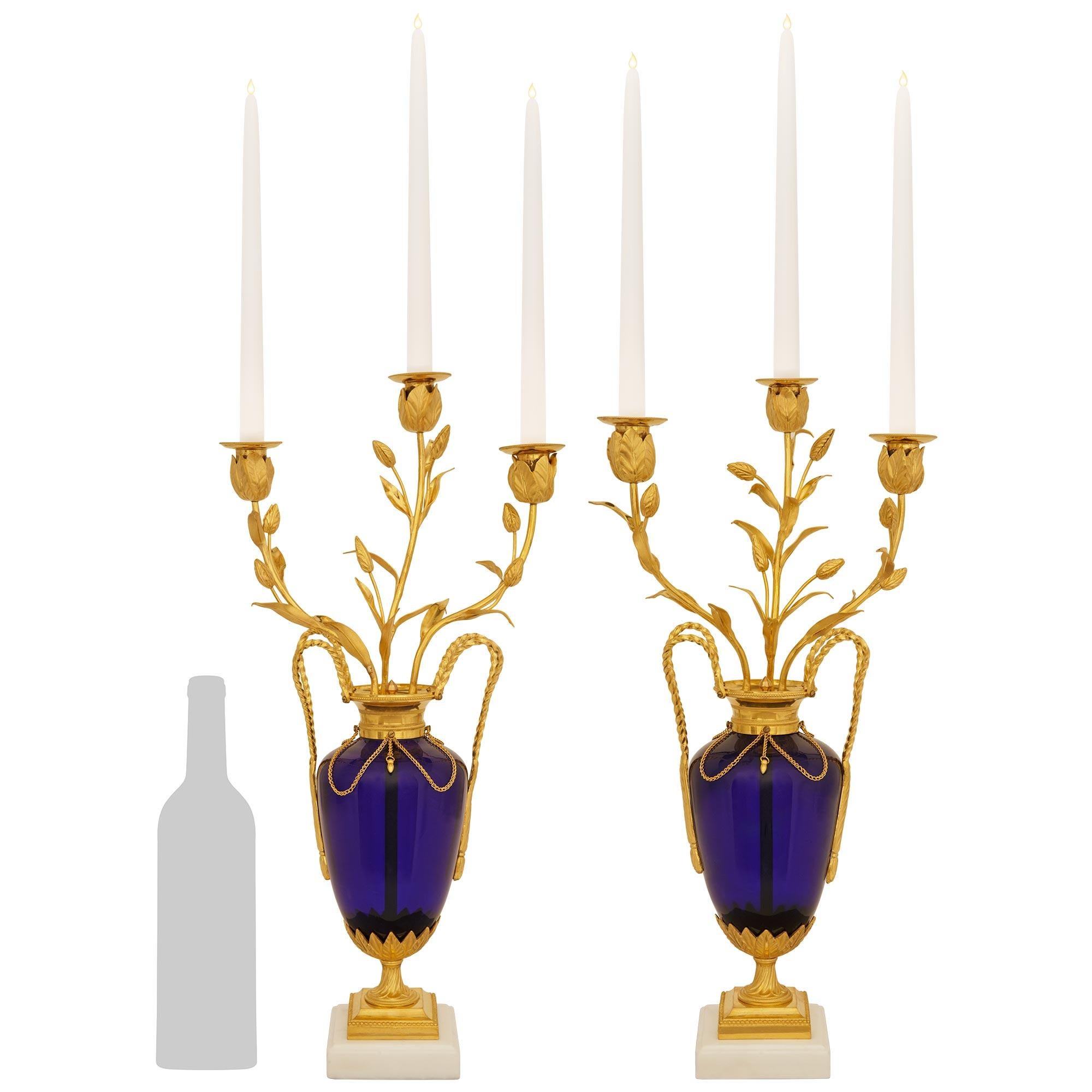 An elegant and high quality pair of French mid 19th century Louis XVI st. Glass, Ormolu and white Carrara marble candelabras. Each stunning three arm candelabra is raised on a white Carrara marble base with mottled edges below a square Ormolu mount