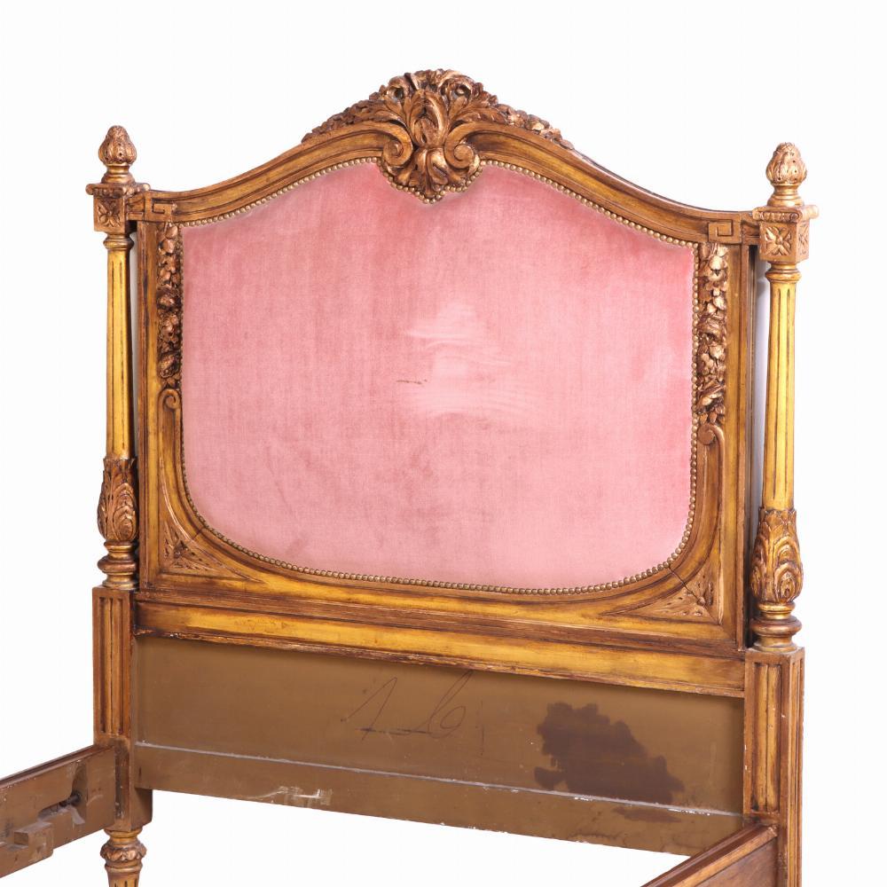 A graceful pair of French twin beds each with a finely carved giltwood frame with classical detailing, including central floral crests, fluted posts, beaded moldings, and rosettes. The upholstered headboards are gently arched. The footboards are