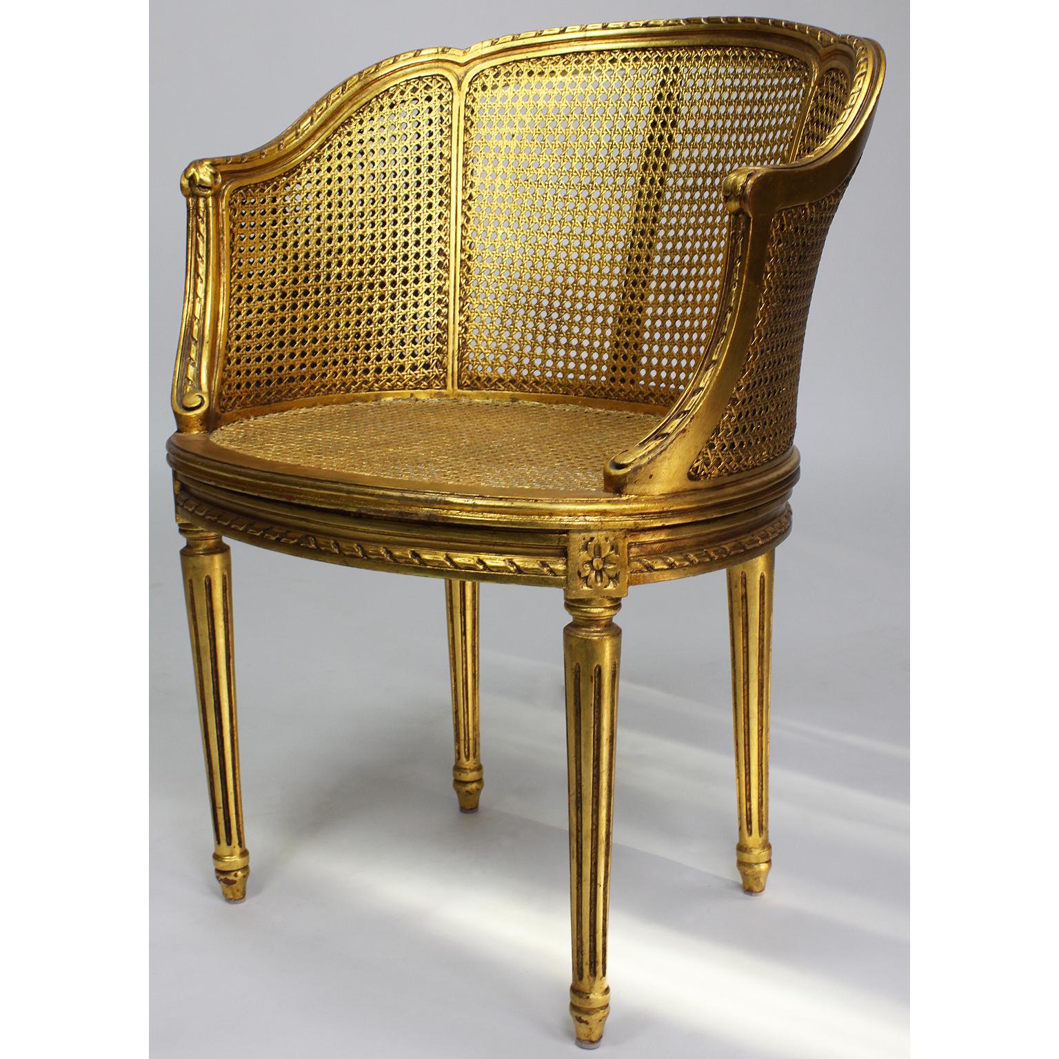 Pair of French Louis XVI style giltwood carved and cane Fauteuils armchairs. The arched back and barrel-shaped frames with a caned back, sides and seat all raised on four fluted legs, circa 1930s.

Measures: Height 31 7/8 inches (81 cm)
Width 24