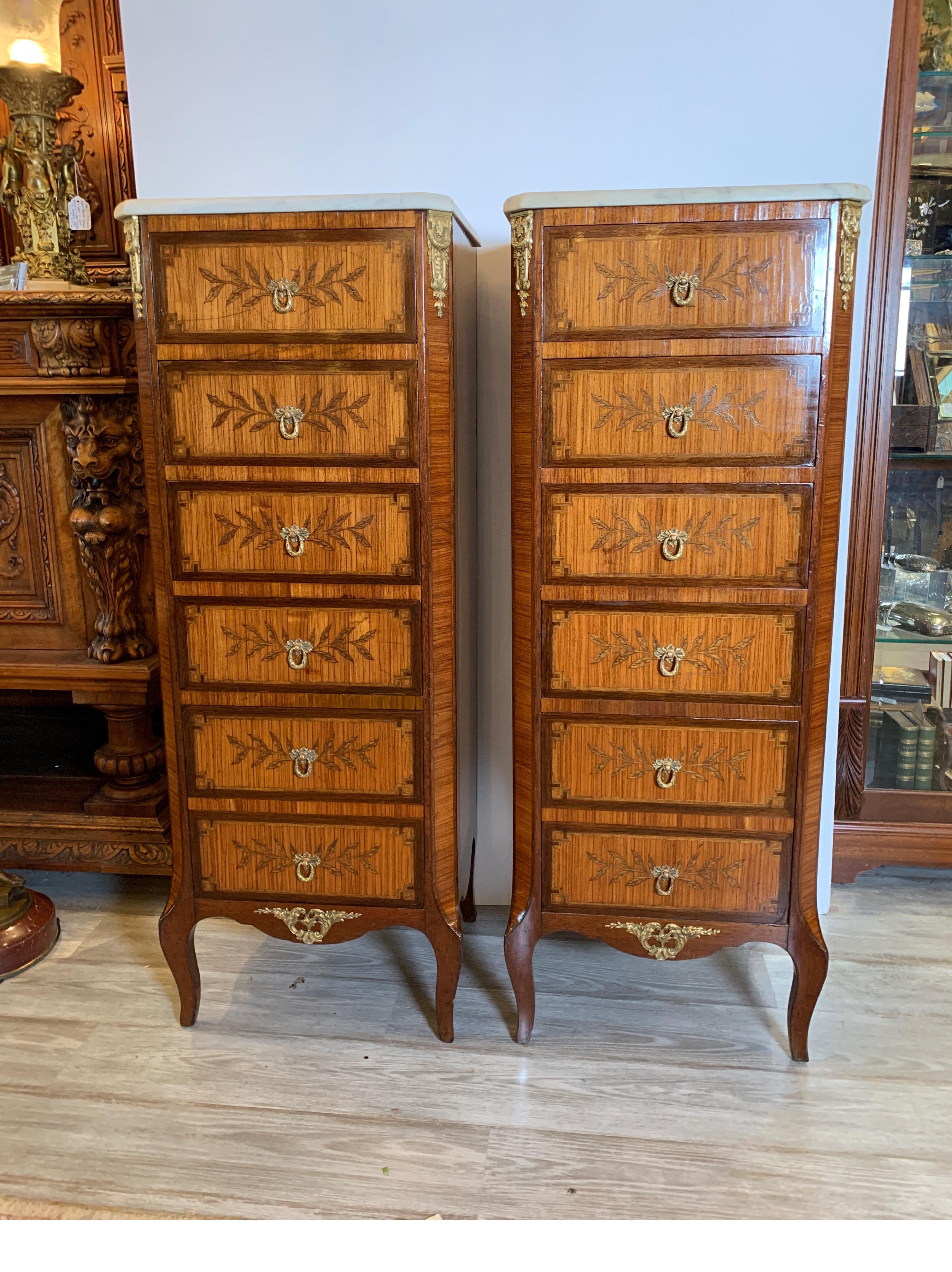 Elegant pair of Classic Louis XV style tall and narrow chests of drawers. The original marble tops resting on cases of inlaid mahogany and tulip wood with ormolu mounts. Six drawers on each tall chest. 48 inches high. Sold by a New York City