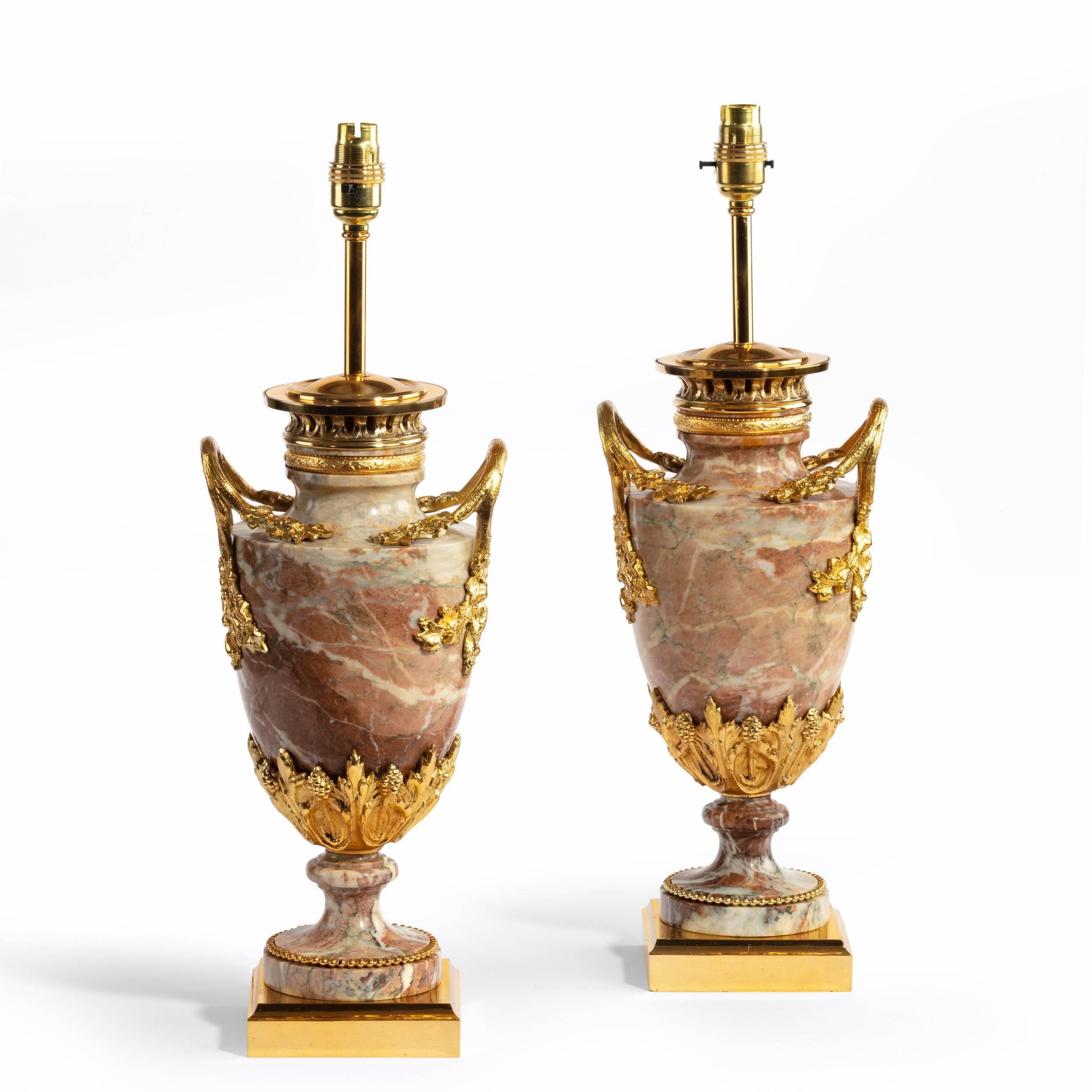 A pair of French marble table lamps, each in the form of a footed vase applied with tall, arched ormolu handles and a band of lanceolate leaves and seed heads around the base, ( adapted from oil lamps for electricity, shades not included.), French,