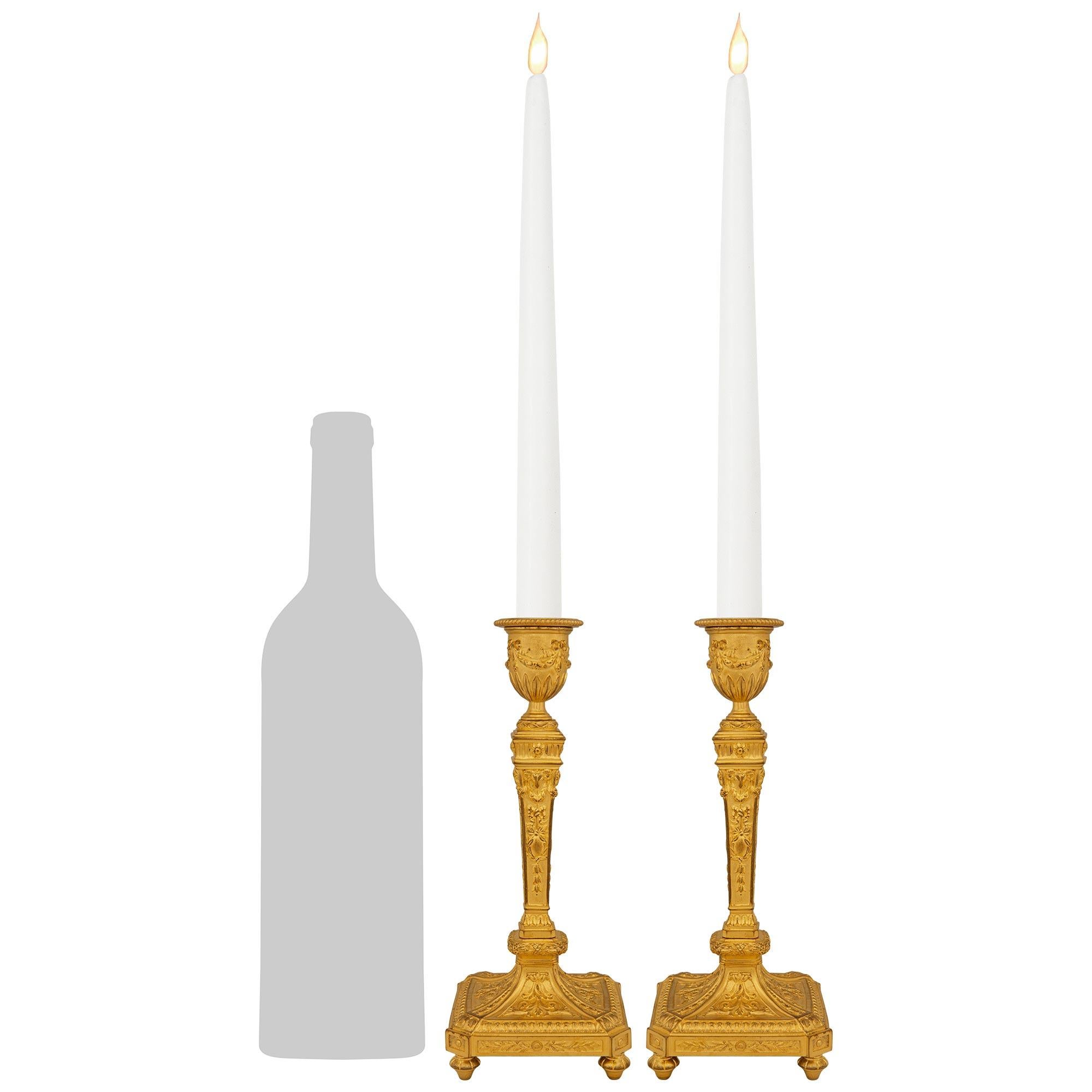 Une paire élégante et très décorative de chandeliers en bronze doré de style Louis XVI du milieu du XIXe siècle. Chaque magnifique chandelier repose sur une base carrée aux coins coupés et est surélevé par des supports en forme de toupie. Les côtés