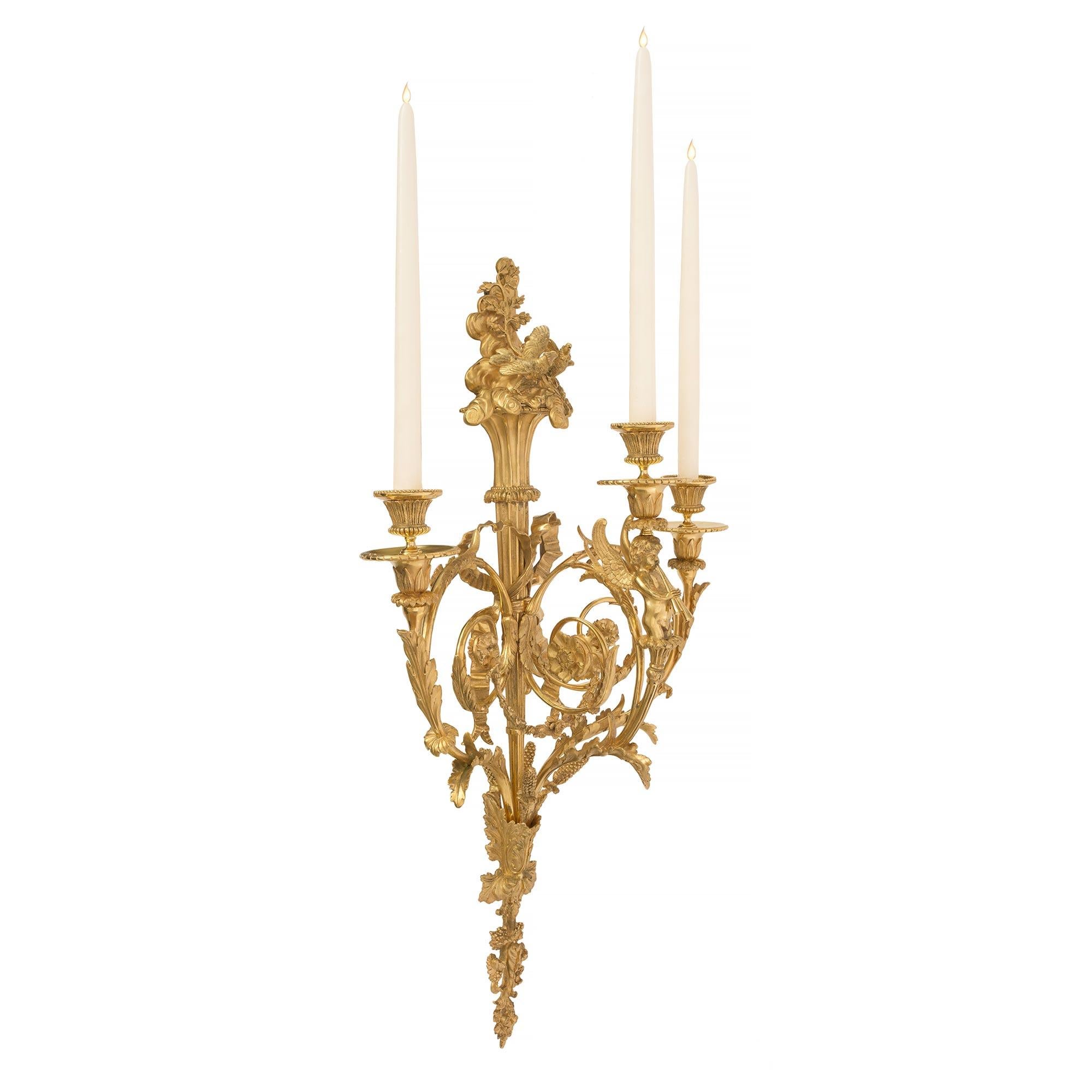 A very high quality and large scale pair of French mid-19th century Louis XVI style ormolu, three arm sconces, “Aux Tourtereaux”, possibly by Henry Dasson, attributed to Pierre-François Feuchère (1737-1823). Each has a bottom pierced finial with