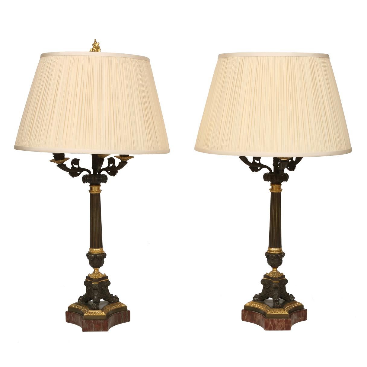 A pair of French Napoleon bronze and gilt metal candlestick lamps with silk shades, on a tripod marble base.