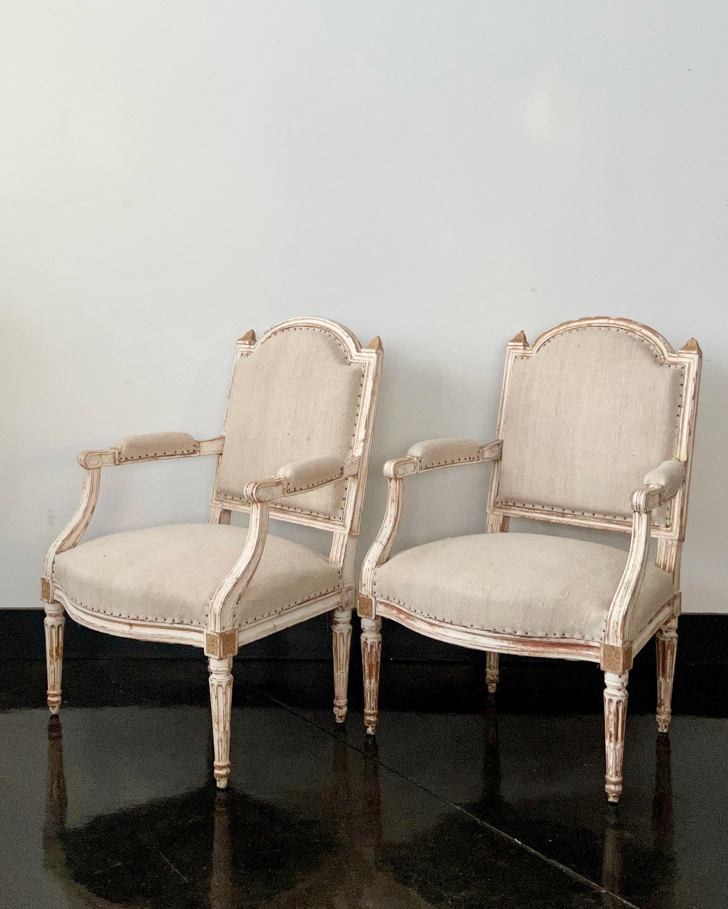 Paire de fauteuils français peints de style Louis XVI en bois massif sculpté, reposant sur quatre pieds fuselés cannelés accentués par des rosettes sculptées sur les joints - montrant par endroits des fragments de bois doré d'origine.
Tapissé de