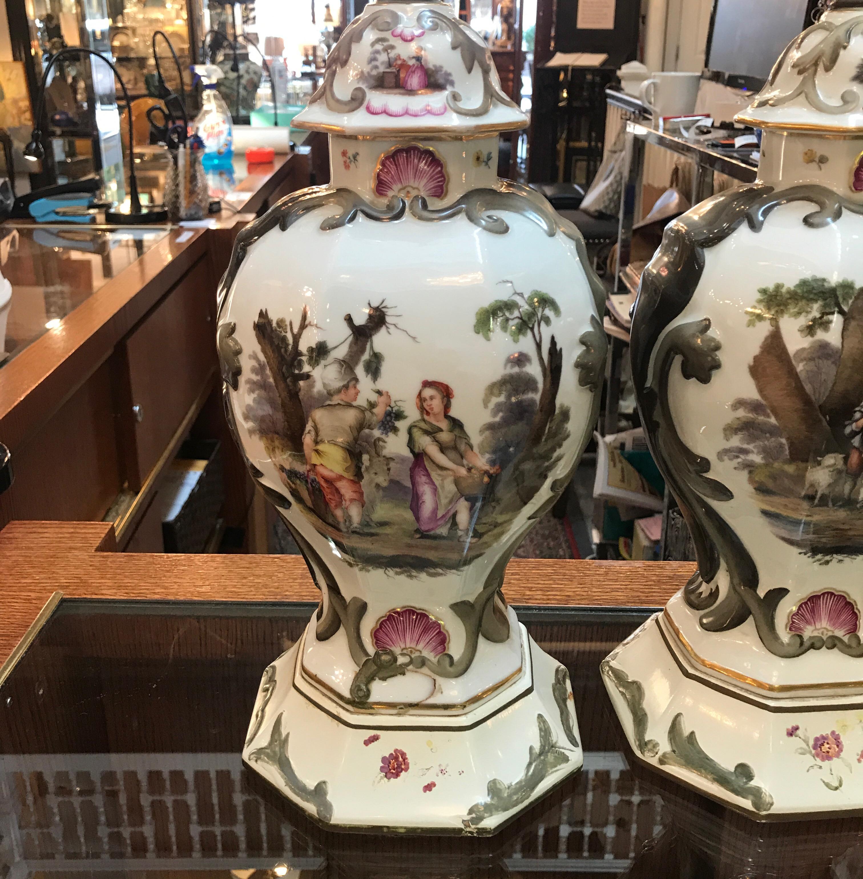 A pair of 19th Century Paris Porcelain urns now as lamps with custom hand pained added bases. The urns with one side depicting children in a lovely bucolic background the other being bouquets of flowers and insects. The simple drum shades are for