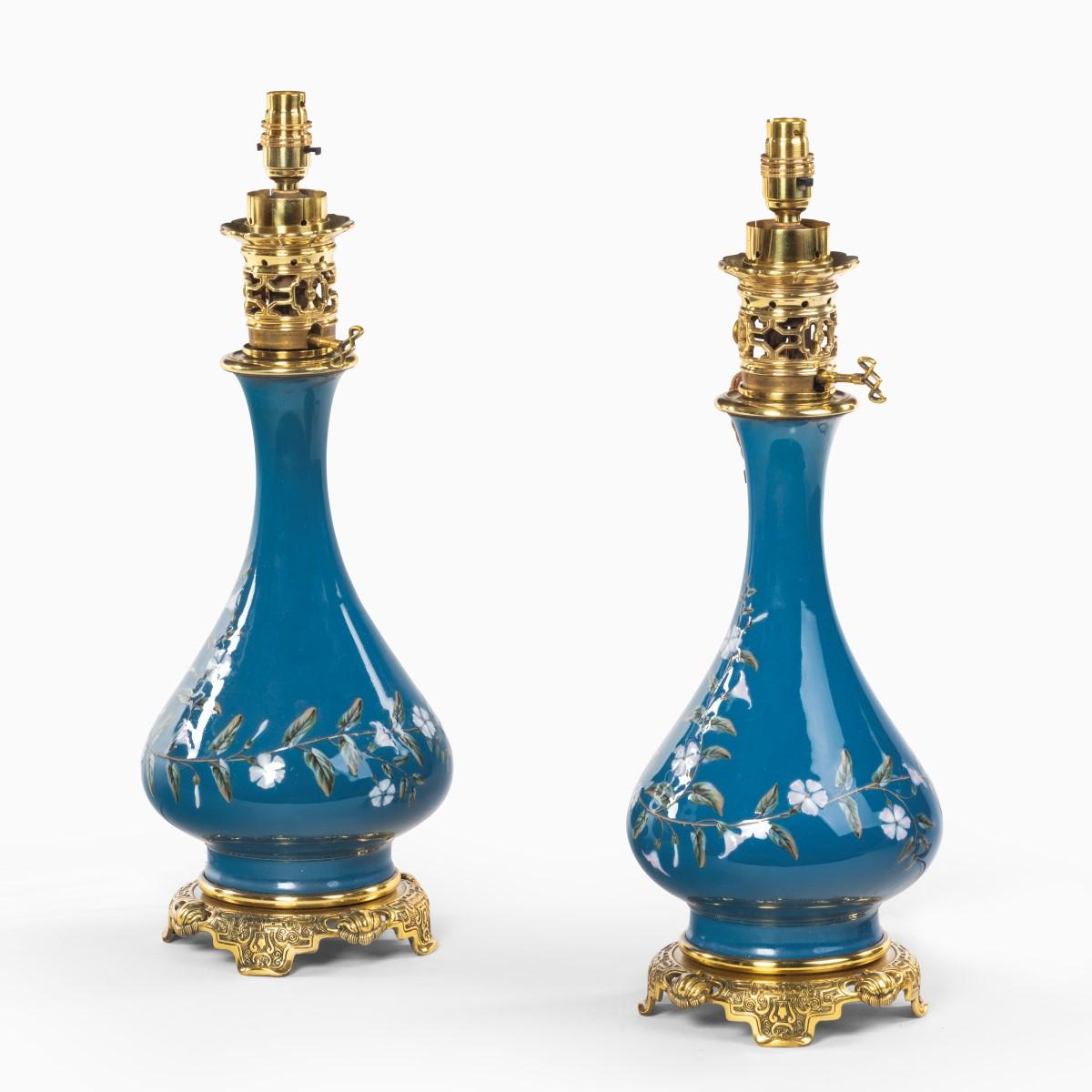 A pair of French pate-sur-pate ceramic oil lamps, of globular form with applied white flowers and leafy tendrils on a blue ground, with high quality ormolu mounts in the Chinoiserie style, now converted to electricity, Circa 1890.

  