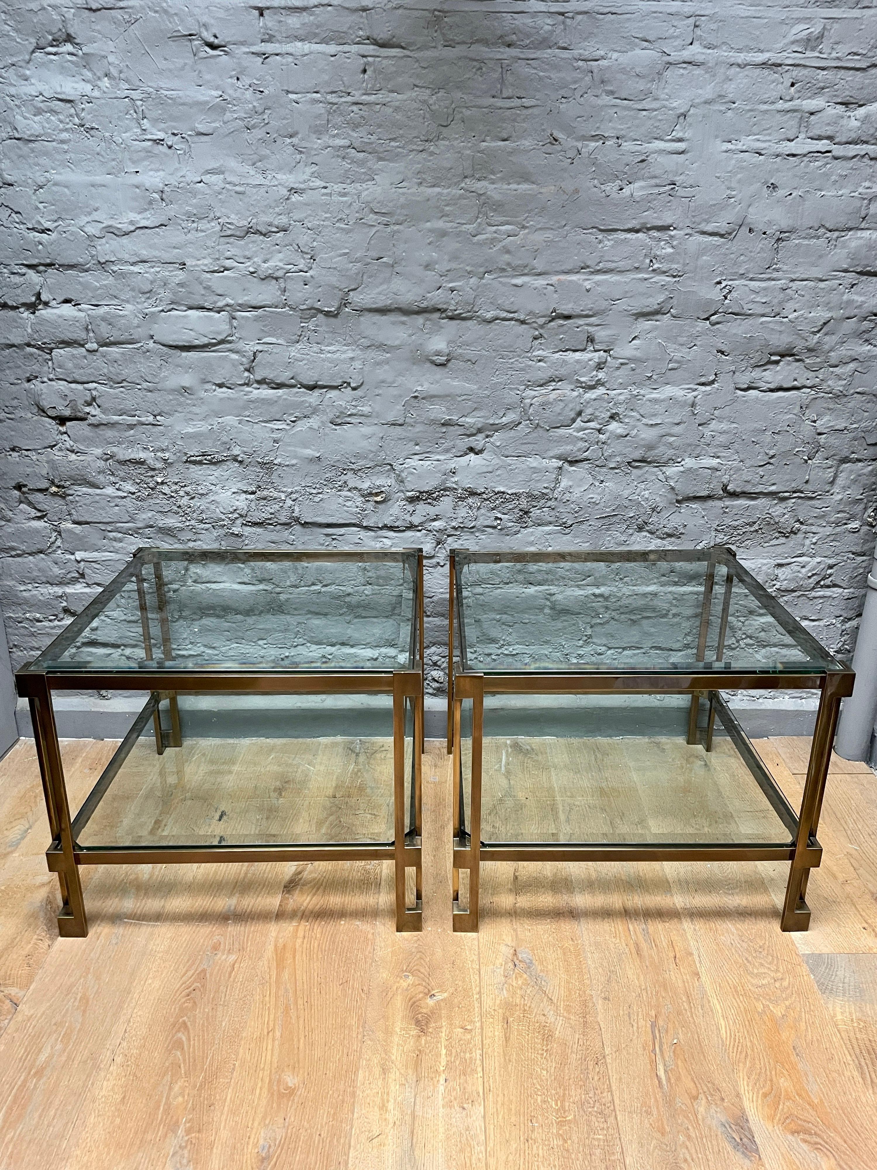 A substantial and very good quality pair of patinated brass two tiered tables, architectural in design with bevelled glass plates. In very good condition with a squared aesthetic, angled columned opened supports. The brass with a bronze colour