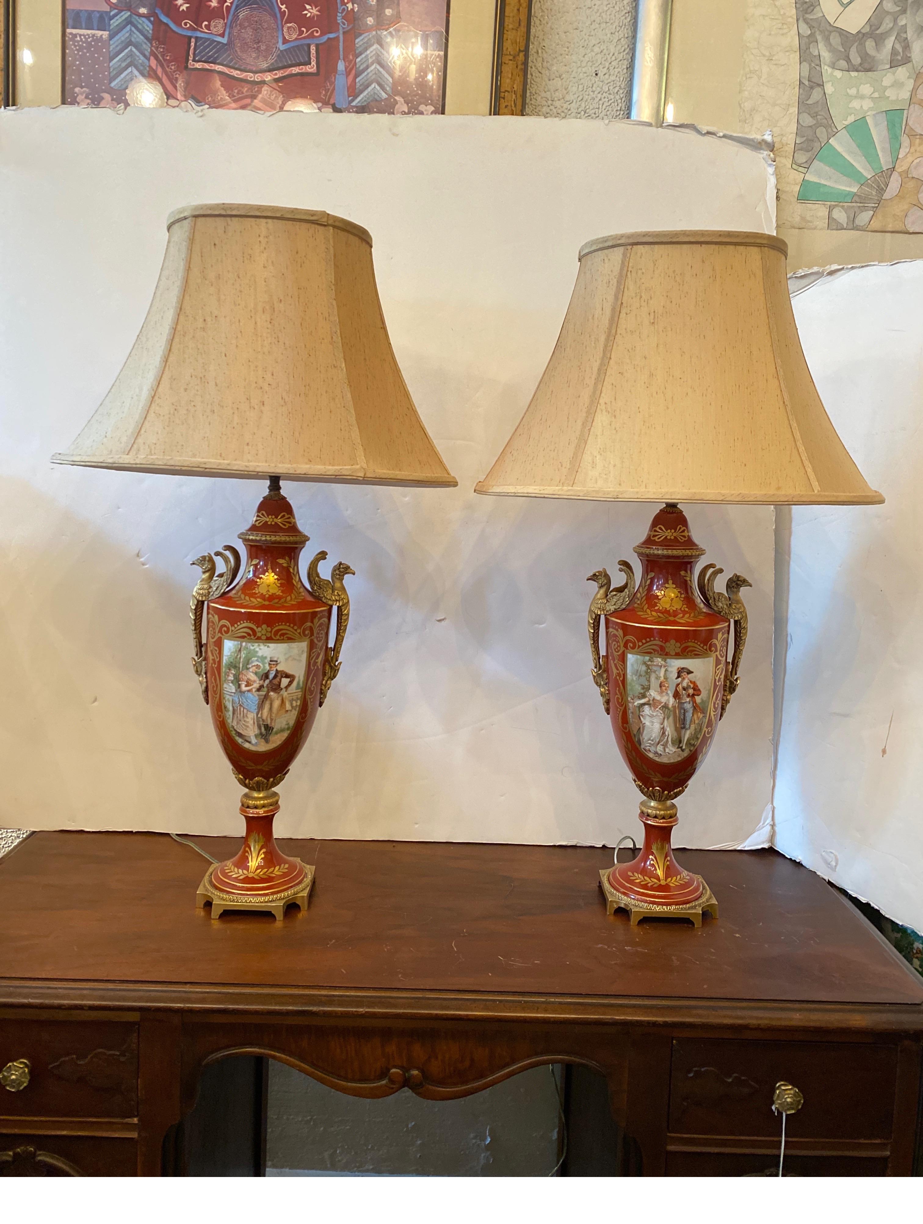 A Pair of French Porcelain Iron Red and gold urn form lamps.  The hand decorated front cartouches with gilt bronze handles and mounts.  The decorated panels with artist signature at the bottom.  These have a pseudo Sevres mark but are Limoges