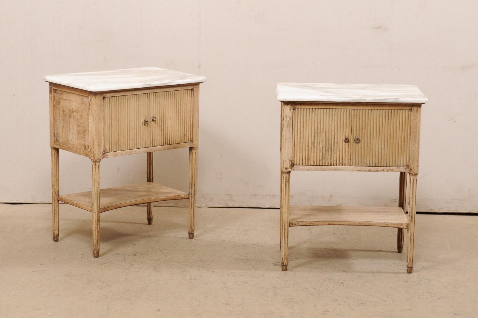 A French pair of side chests, with lower shelf and marble tops, from the mid 20th century. These vintage side chests from France each retain their original marble tops, which rest atop a thick apron which is fitted with two reed-carved doors, and