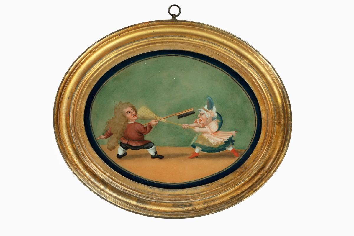 A pair of French reverse glass paintings or cartoons, each of oval form, one depicting a man with a mass of hair or full wig using a brush to fence with a woman wielding a broom, the other with two characters fencing, both wearing tricorn hats and
