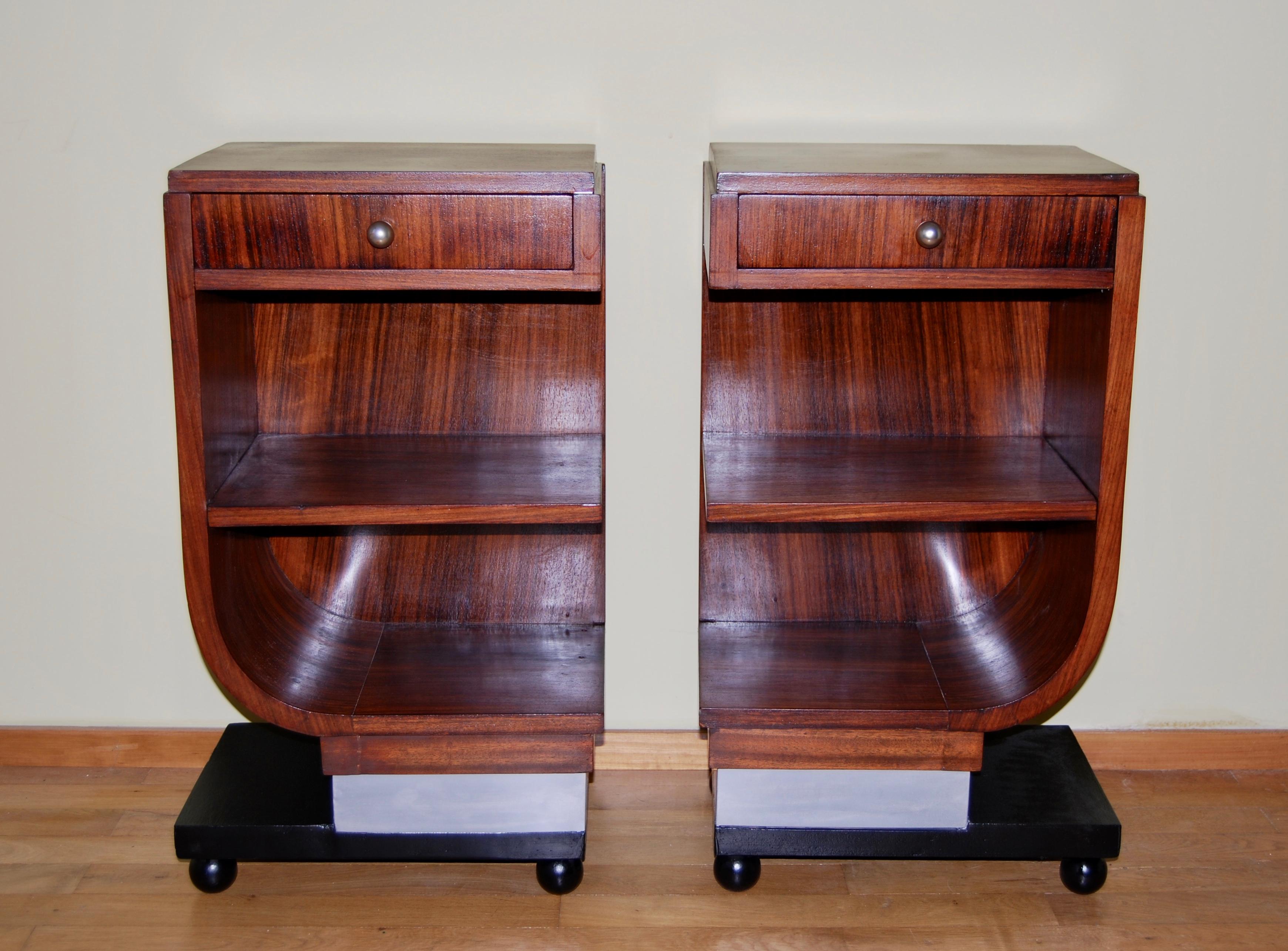 Beautiful pair of asymmetrical French Art Deco bedside tables.
In Rosewood veneer each has an opening drawer with original steel ball drawer handle & 2 shelves
The base is a chrome coloured plinth with black wooden support on ball feet.