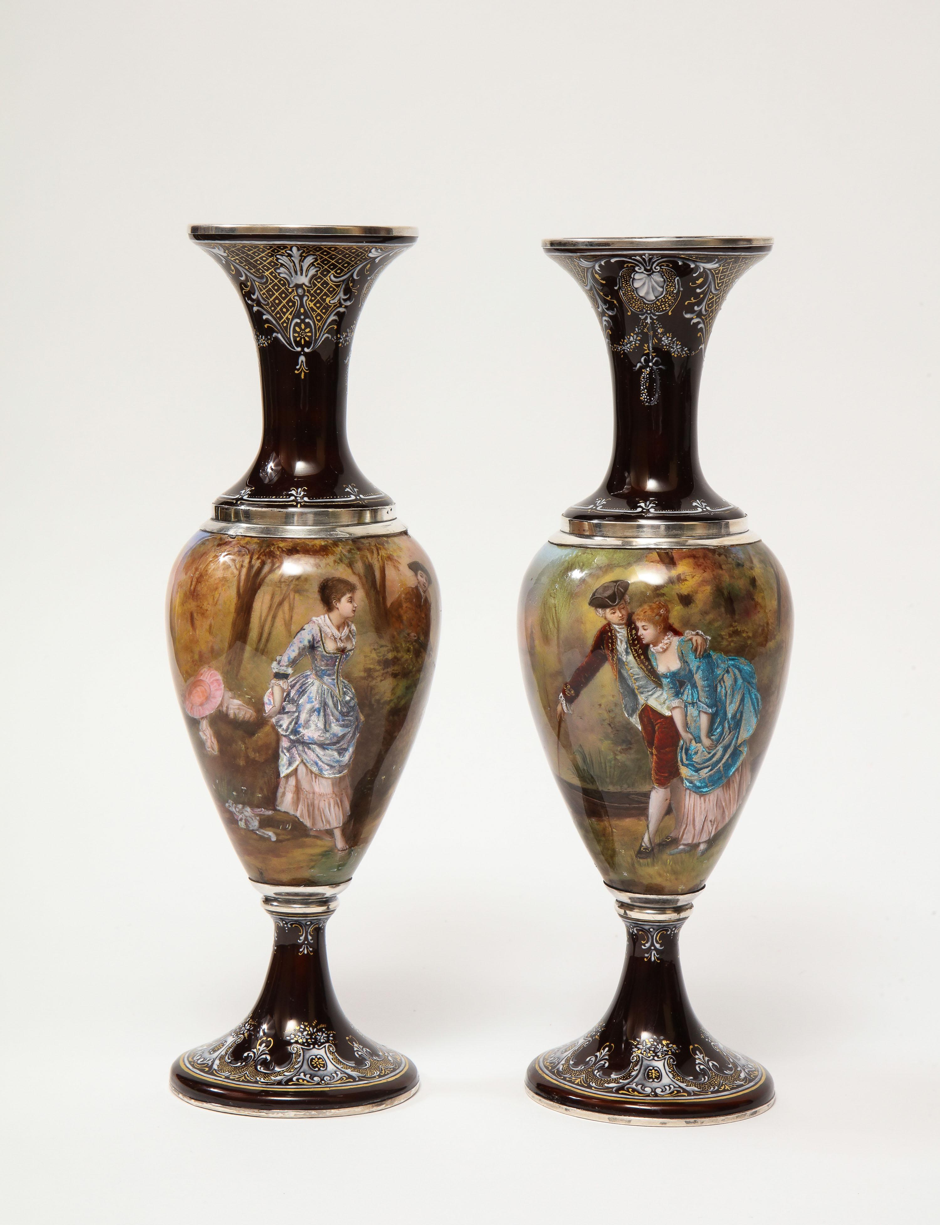 A pair of French silver & Limoges enamel vases, retailed by Tiffany & Co., 19th century.

The silver mounts with JC hallmarks, for Joseph Cousin, Paris.

The first painted with a couple next to a rowboat with a castle in the distance, the second