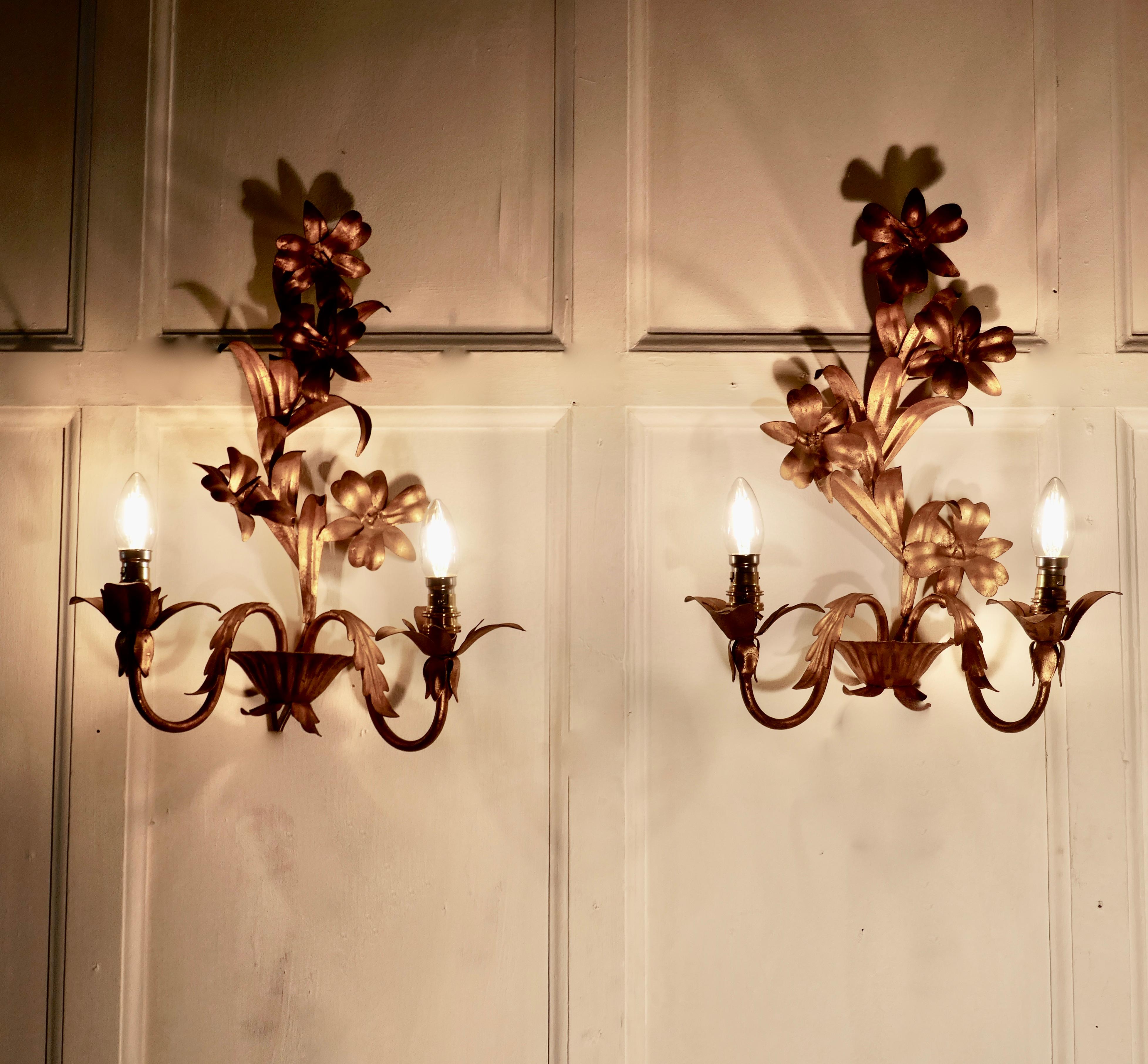 A pair of French two branch toleware gilded wall lights

These are very pretty two branch wall lights, the brass sconces are decorated with flowers and curled leaves
The lights are all working and will need to be installed by an electrician
The