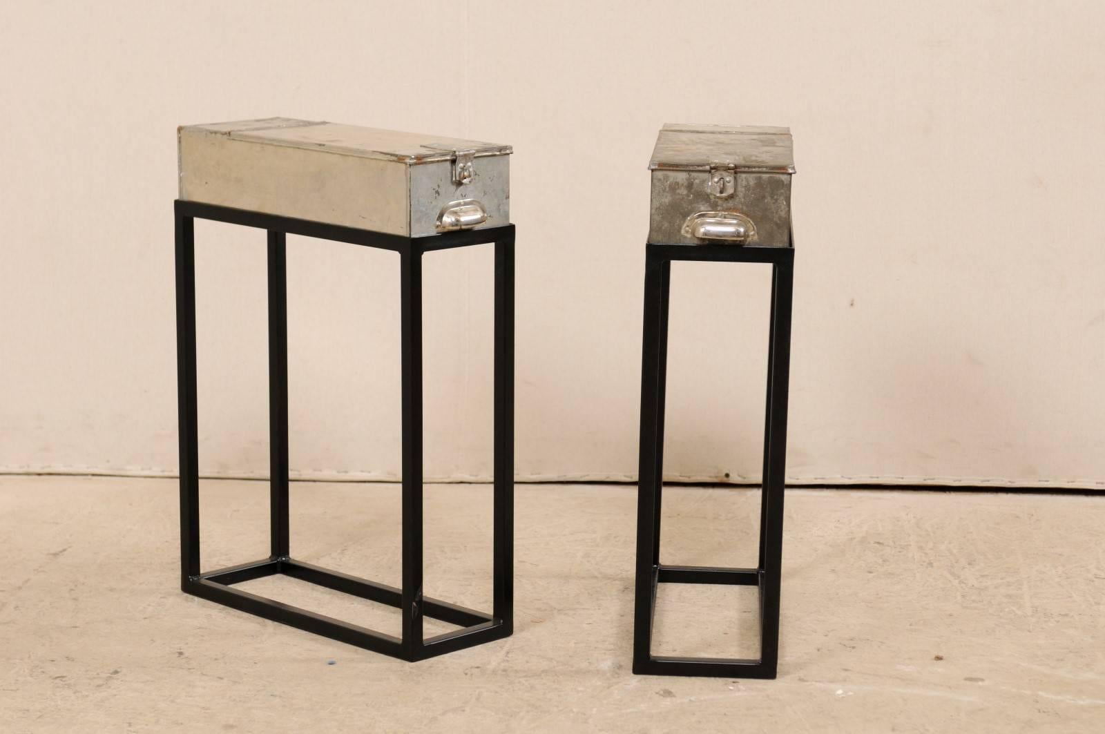 A pair of French vintage bank boxes on custom stands. This fun and whimsical pair of drinks or side tables have been fashioned out of vintage French silver metal bank boxes, re-purposed as tops, and set onto a custom black metal base. The tables