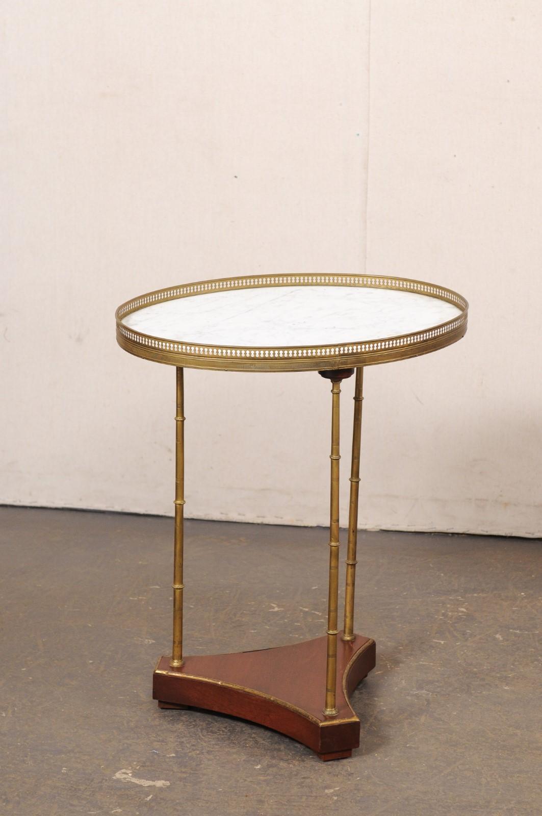 A French pair of oval side tables, with marble and brass gallery edge top, from the mid 20th century. These vintage tables from France each have an oval-shaped top with white marble surrounded within a brass gallery style perimeter edging. The top