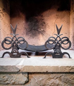 A pair of French wrought iron fire dogs in the style of Gilbert Poillerat