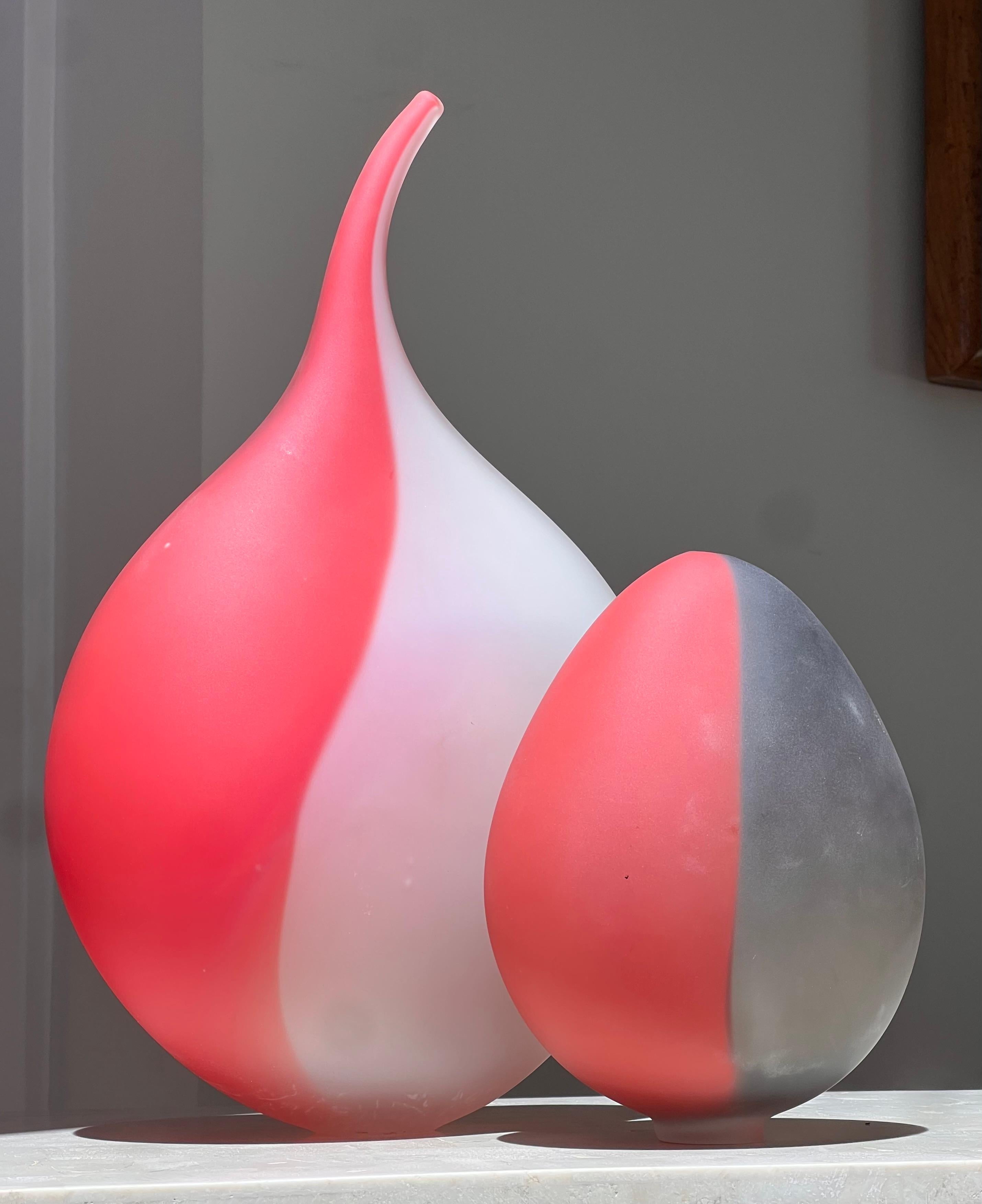 A pair of frosted art glass vessels, 20th century. The taller boasts tones of cadmium red and snow, whilst the shorter is cadmium and pewter. Each has a tiny opening at the mouth which might fit the most narrow of stems, though these are gorgeous as