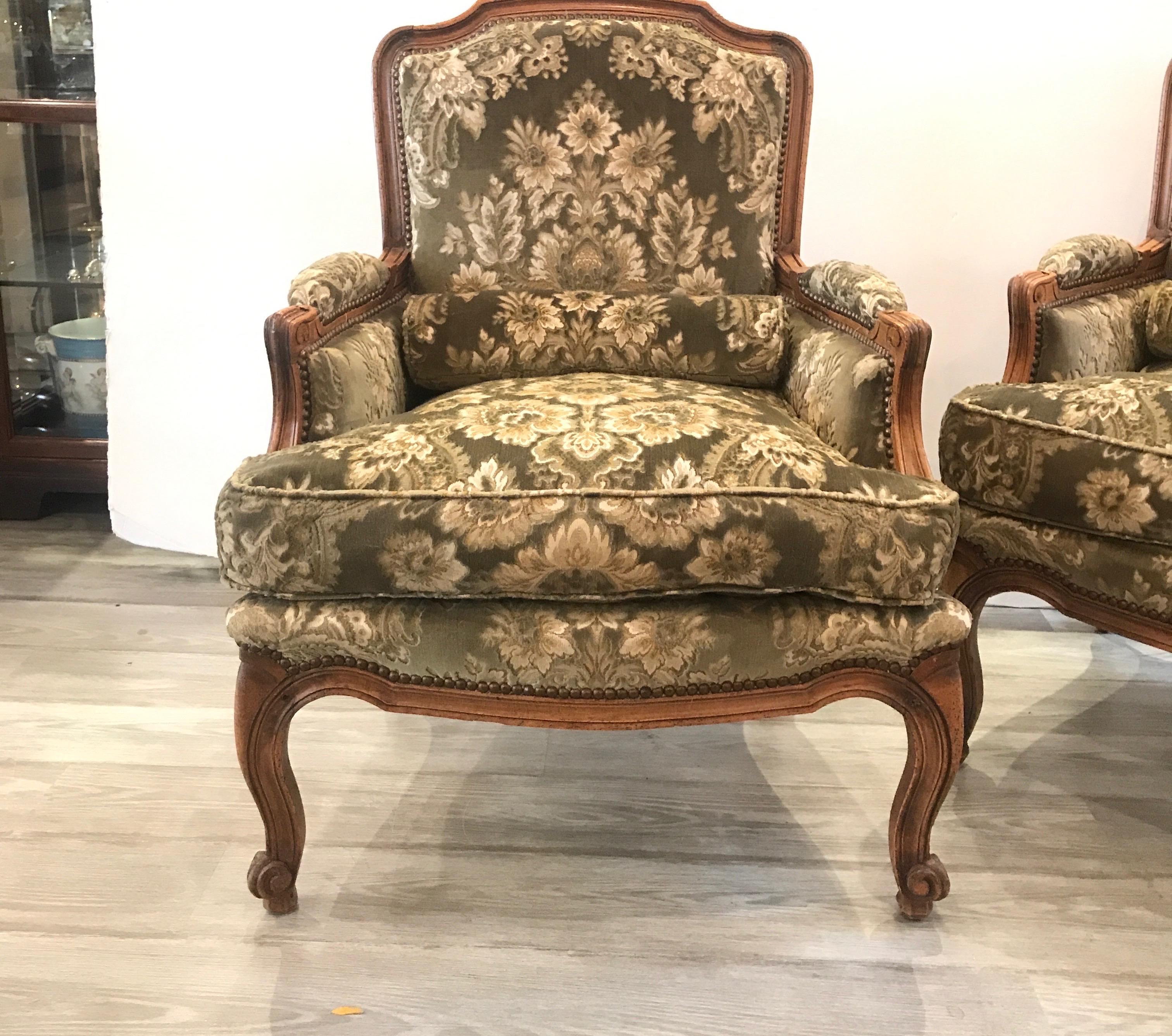 Beautiful pair of bergère chairs with hand carved details. The medium wood color fruitwood frames with new high end Italian damask pattern cut velvet upholstery. The attached back with loose cushion seat with small round lumbar pillow. The cushion