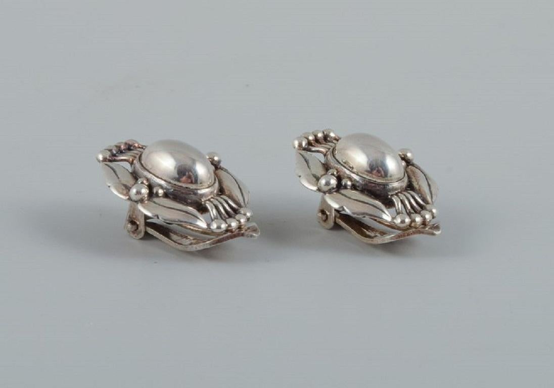 A pair of Georg Jensen ear clips in sterling silver.
Jewelery of the year 2000.
Marked.
Measurements: L 20mm x D 15mm.
In excellent condition.

Our skilled Georg Jensen silversmith/goldsmith can polish all silver and gold so that it appears as new.
