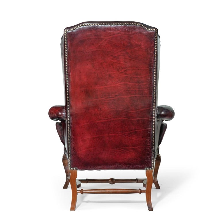 A pair of George I style walnut wing arm chairs, each of typical form with a high back, scroll arms and separate seat cushion, set on four cabriole legs with shaped square section stretchers, reupholstered in distressed burgundy leather. English,