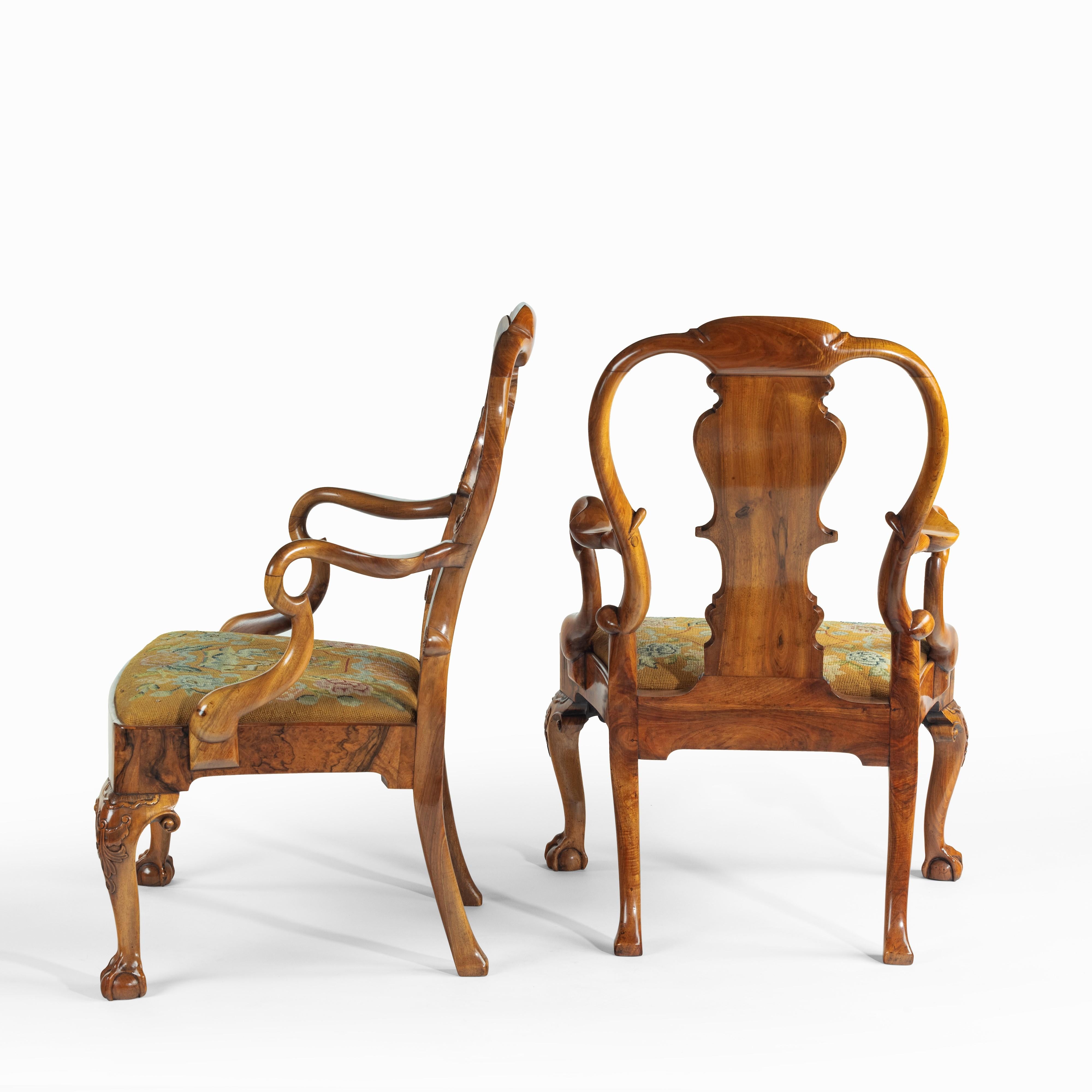 A pair of George II style walnut open arm chairs, possibly by Charles Tozer, each with a high arched back, burr walnut vase splat and shepherds crook arms, the generous drop-in seat with the original needlework, the serpentine seat rail with a