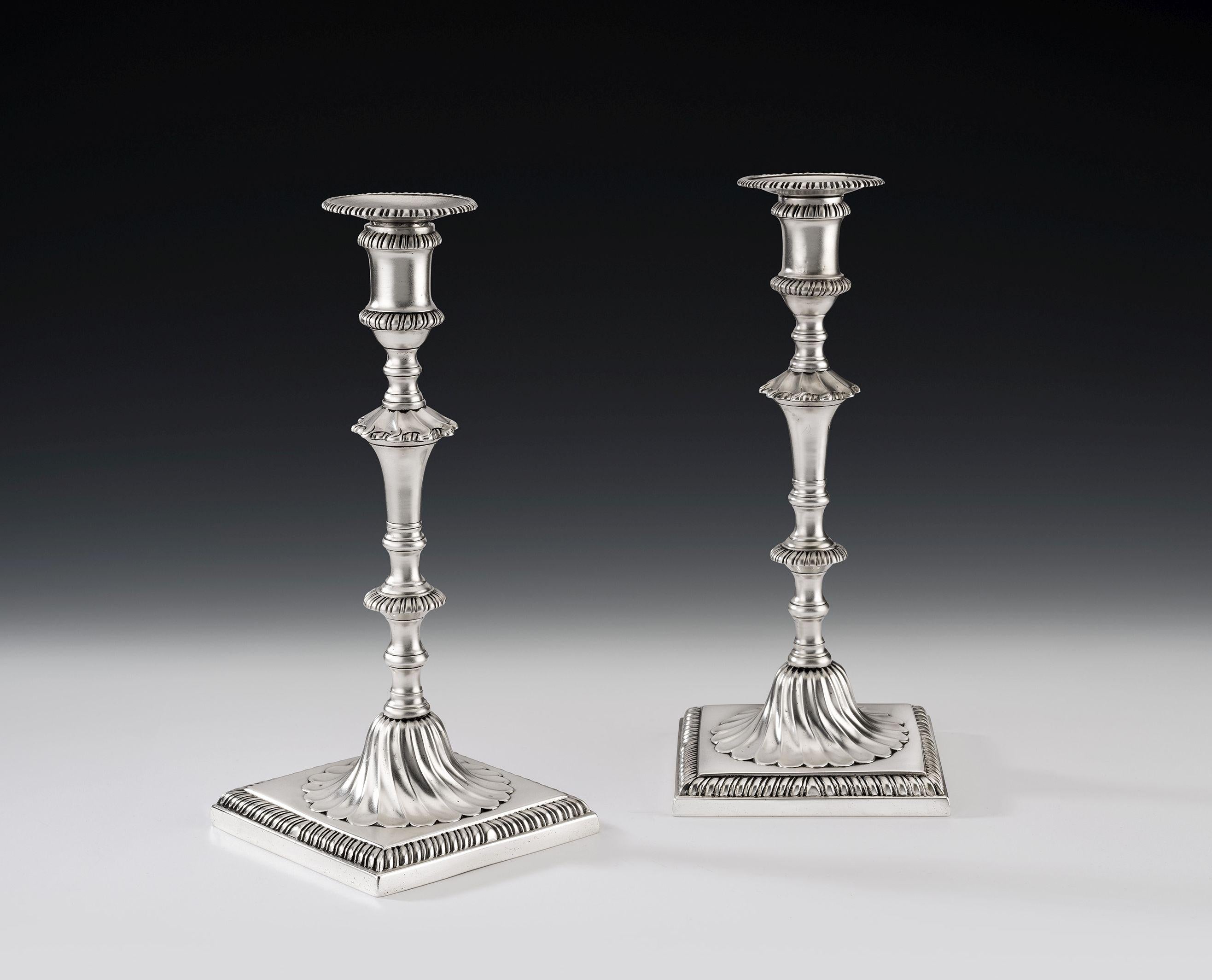 The candlesticks are cast and stand on a square foot decorated with gadrooning. The base displays an unusual domed section decorated with swirl flat fluting and rises to a shaped baluster shaft decorated with gadrooned bands and swirl flat fluting.