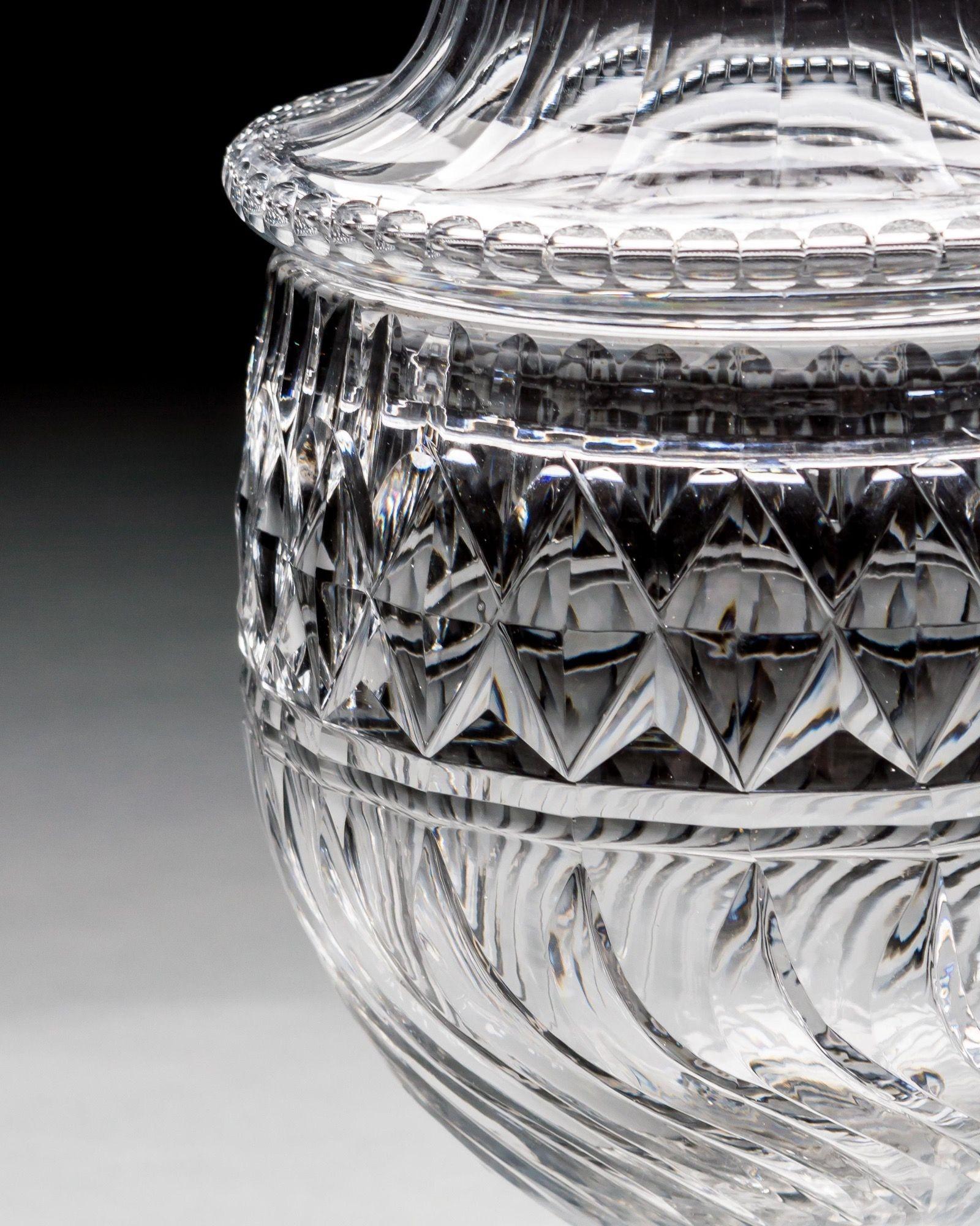 An exceptional pair of Georgian two pieces urns on star cut pedestal foot with scalloped edge, supporting swirl cut bodies with diamond band and pillared rim, fitted with slice cut lids also with diamond bands and swirl cut finials.