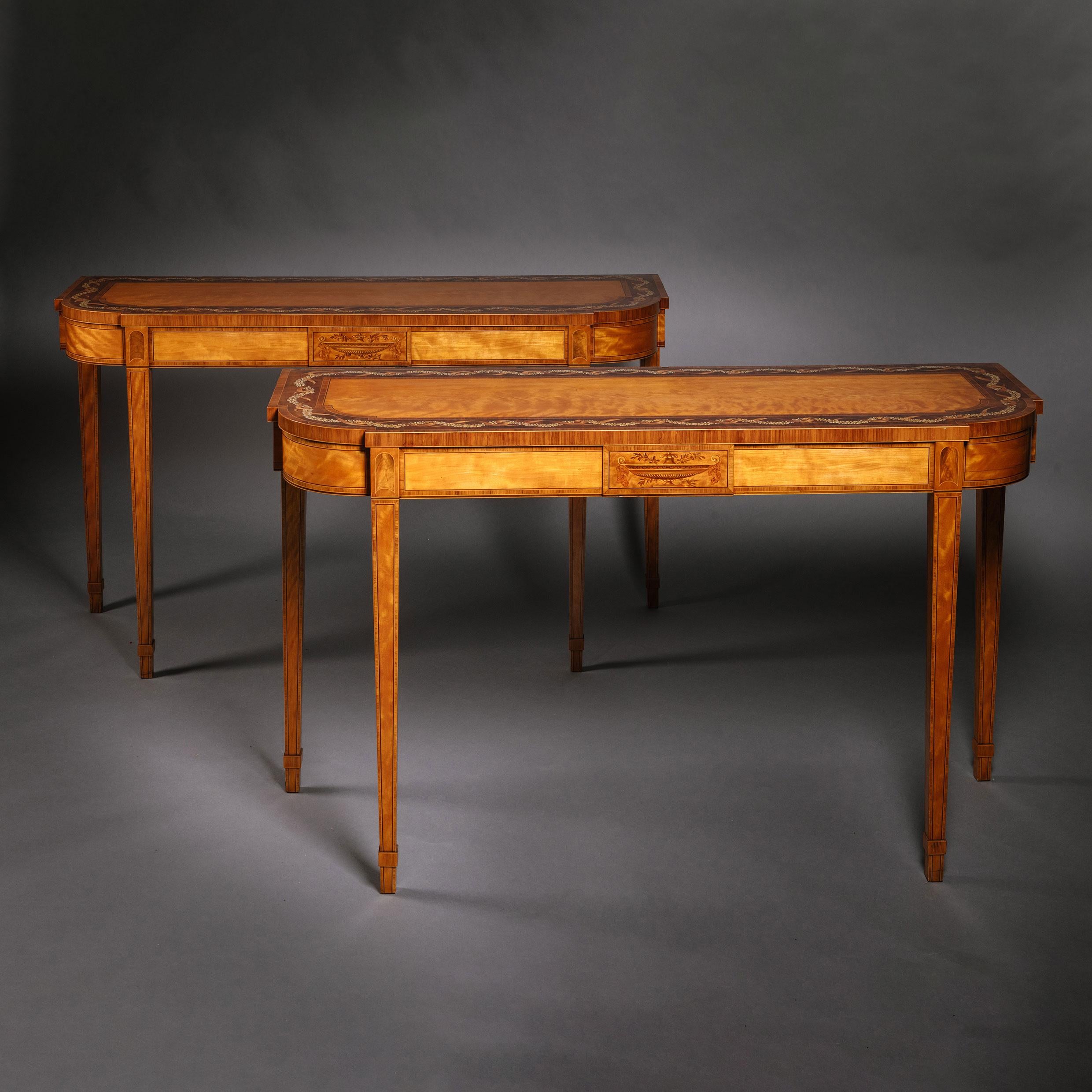 A pair of George III Polychrome-decorated satinwood console tables.
In the manner of Seddon, Sons and Shackleton.

Each with a rectangular top with rounded front corners and painted with a border of ribbon-entwined foliate garlands. The panelled