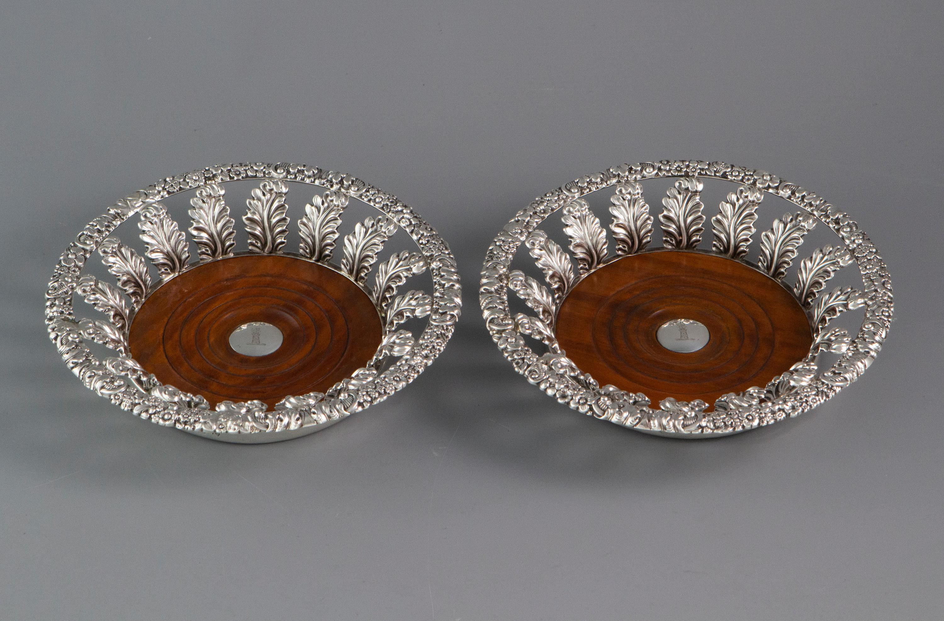 An exceptionally good pair of Georgian silver wine coasters of flared form with cast flowerhead and scrolling foliate rims supported by embossed leaves. Turned fruitwood bases with the central silver button engraved with the crest of a dragon