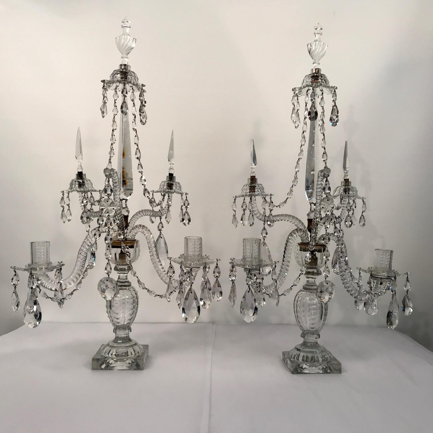 An important pair of two light cut glass brass mounted George III candelabra by the celebrated maker William Parker,
Each raised on a cut baluster and square base supporting two candle arms with hung drip pans and sconces, also with two