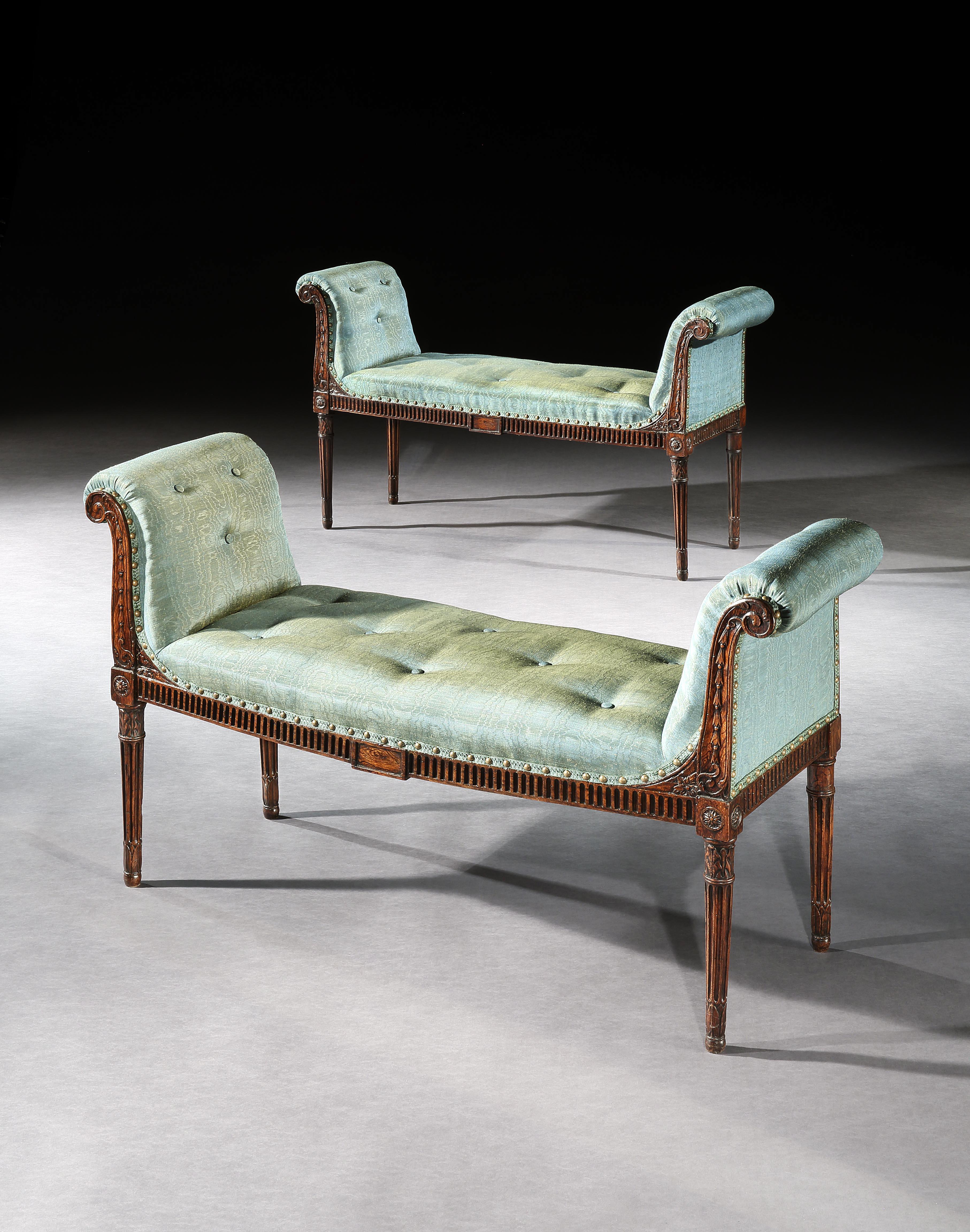 A particularly elegant pair of George III simulated rosewood window seats, the out scrolling arms carved with bell flowers above a carved fluted frieze with a central tablet, and standing on carved fluted legs, headed by paterae and