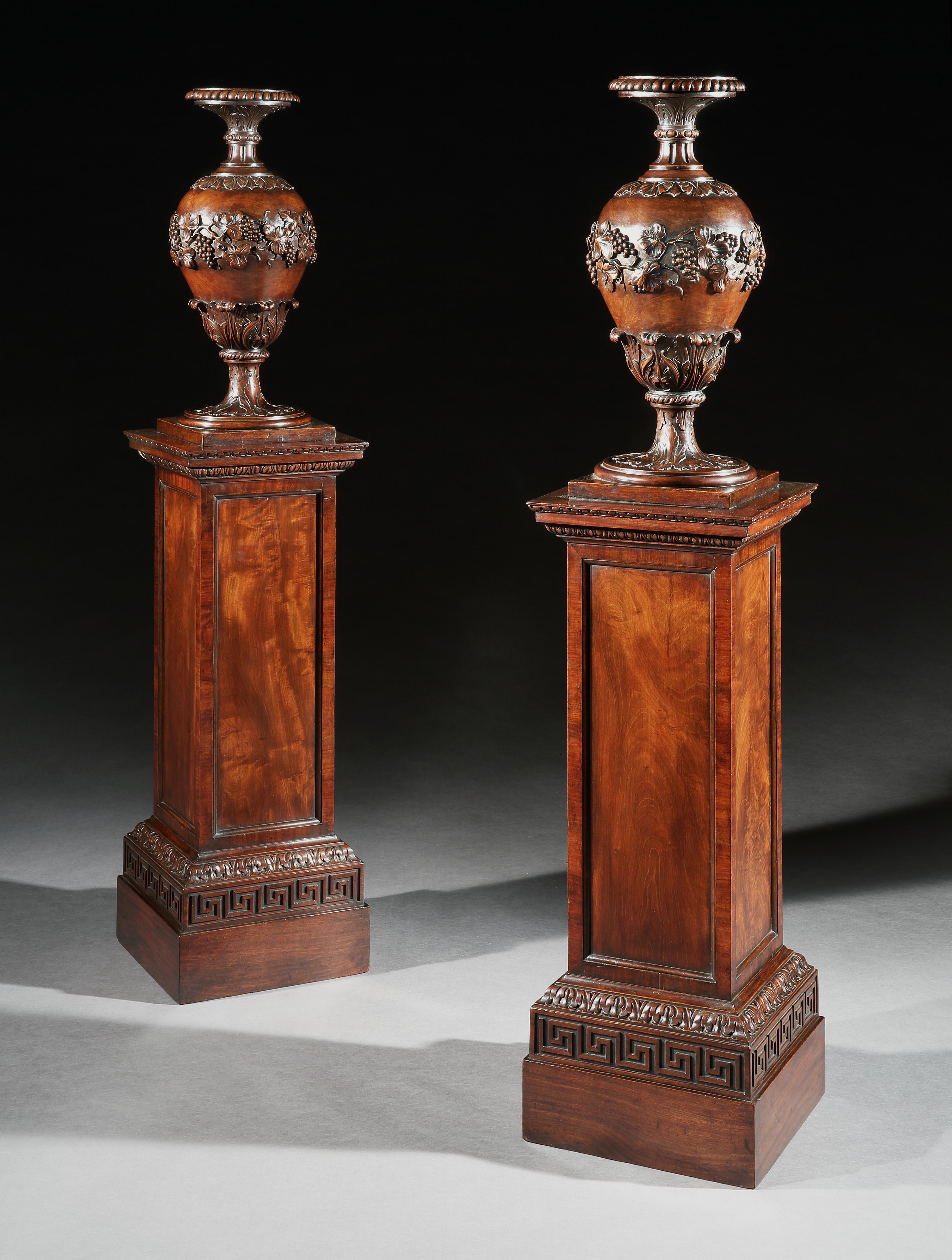 A rare pair of George IV mahogany torcheres, the upper sections having superbly carved urns of acanthus and bunches of grapes hanging from the vine leaves, above a well figured paneled plinth base carved with acanthus, egg and dart moulding's as