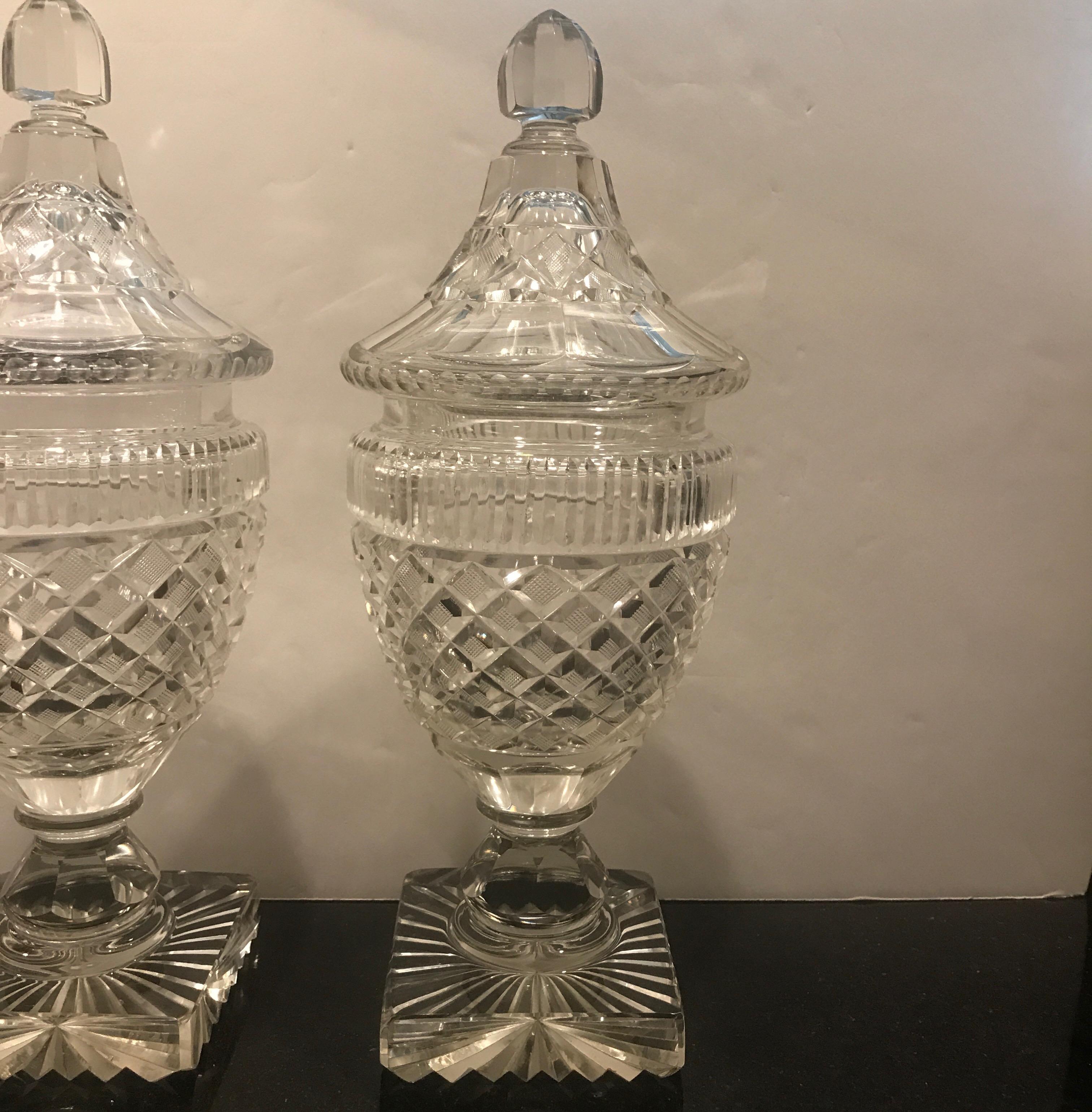 A pair of Georgian period cut class covered sweet meat jars. The lids with panel cut finials with cross cut diamond pattern over slice cut rims and diamond cut urns. The bases with pedestal and starburst bottoms. 11 inches tall. Excellent condition