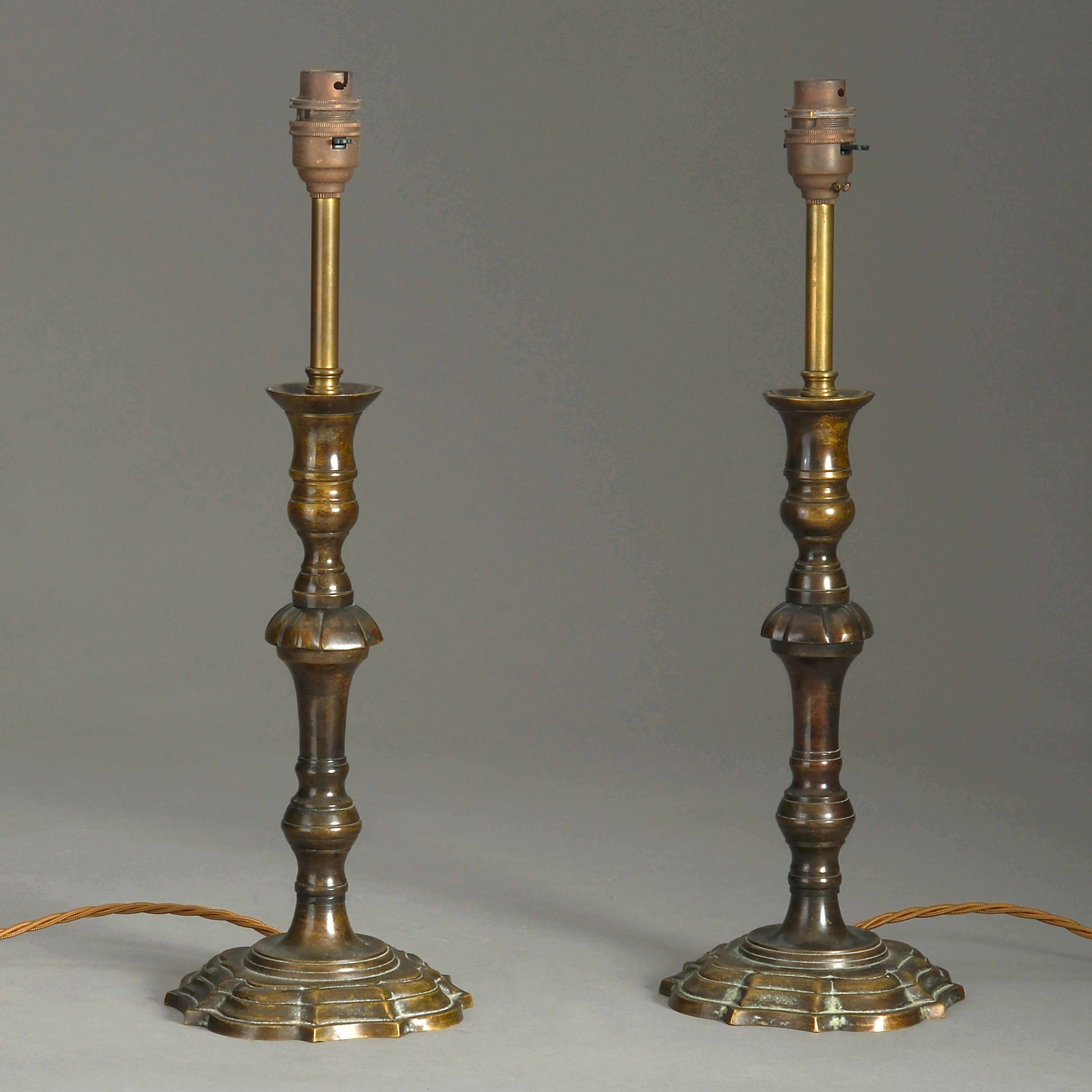 A pair of early 20th century bronzed candlesticks in the George I manner, wired as table lamps.

Wired for electric lighting according to UK safety standards.

These lamps can be rewired for US, EU and Worldwide standards