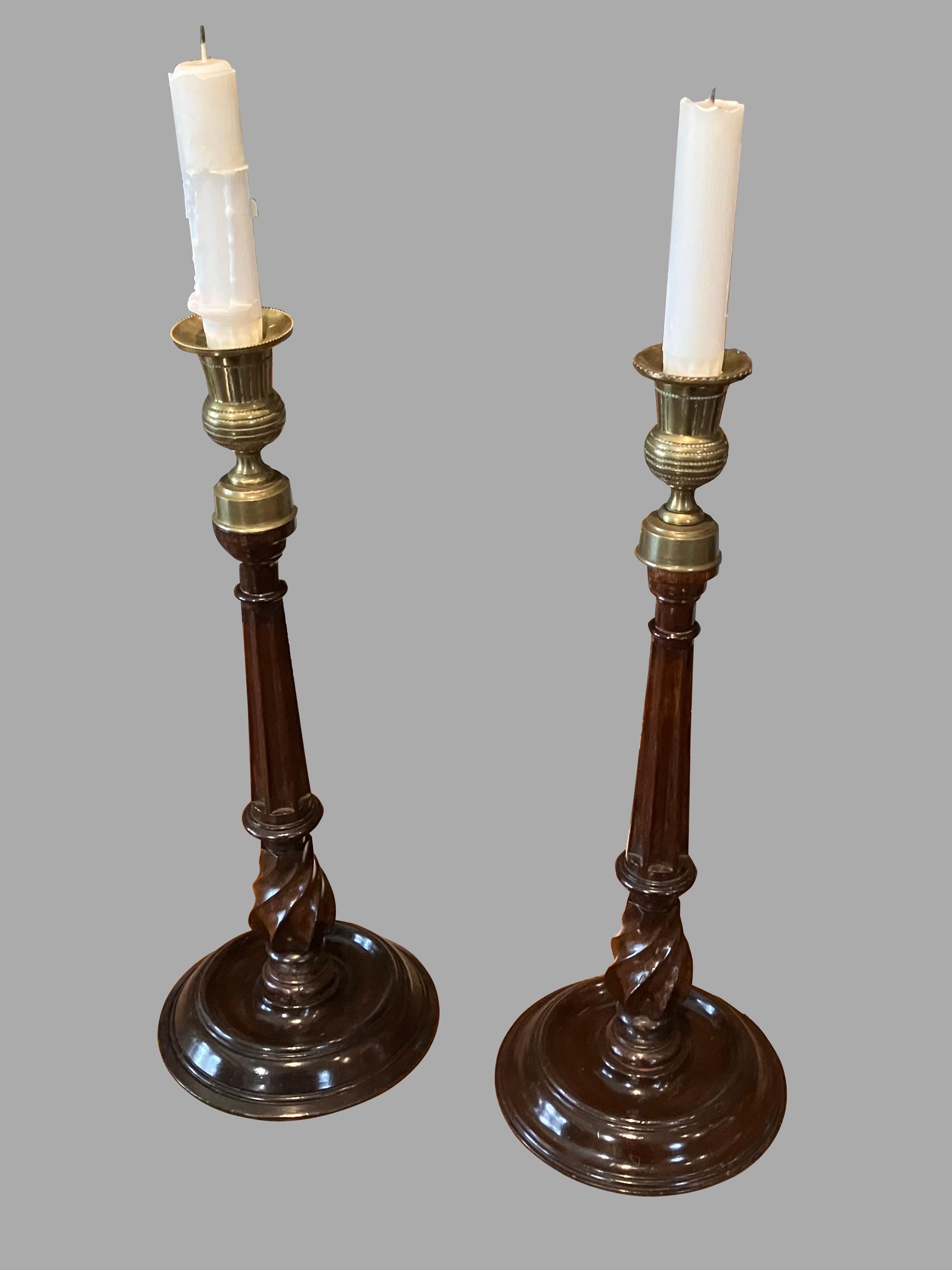 A good pair of English Georgian style mahogany and brass candlesticks, the brass nozzles supported on reeded mahogany columns ending in turned circular bases. This style of candlestick first appeared in the 18th century and has remained popular ever