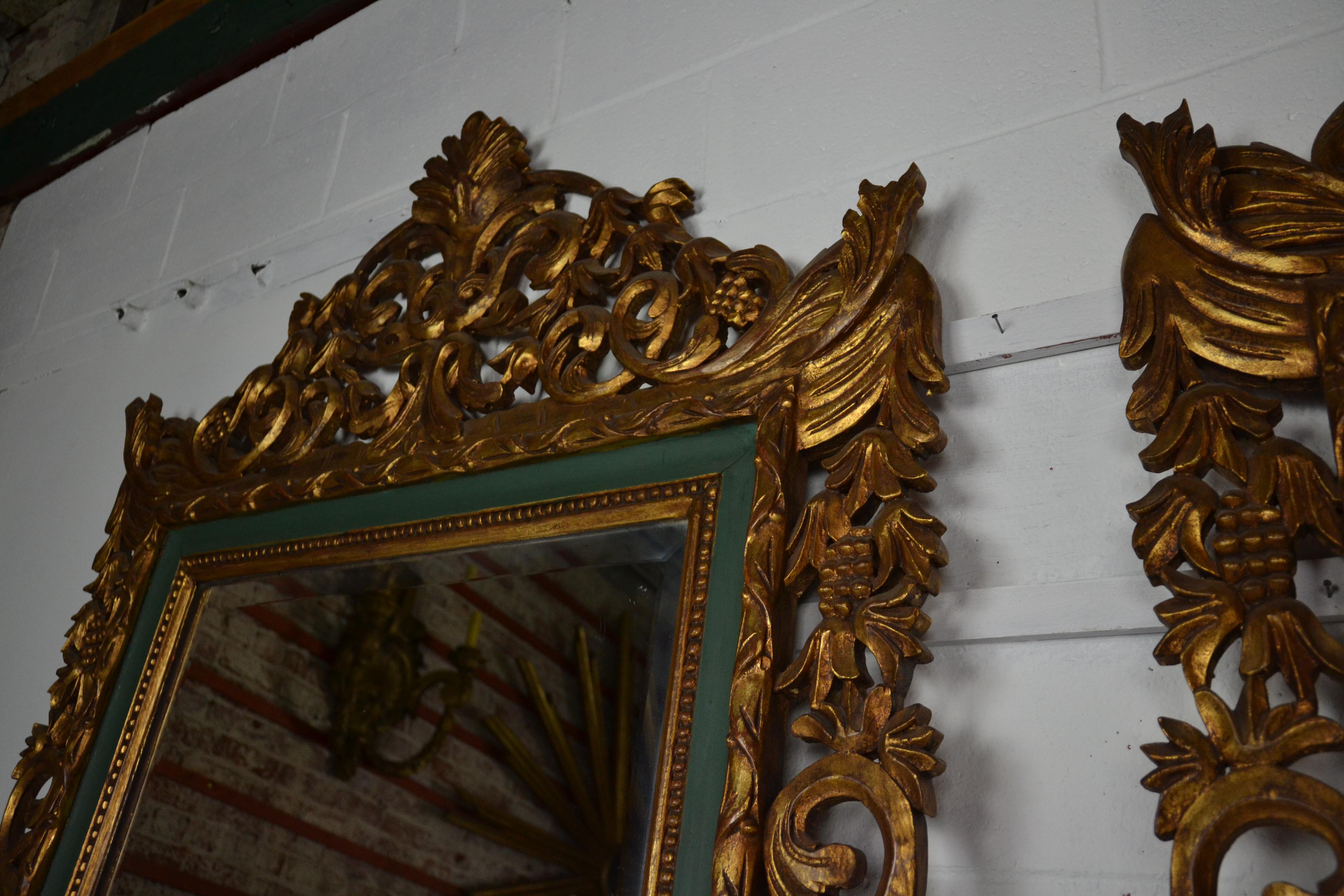 A large pair of hanging or floor standing mirrors with a gilt and green painted finish. Heavy scroll and acanthus leaf carving topped with a shell motif. Wooden plank backed.