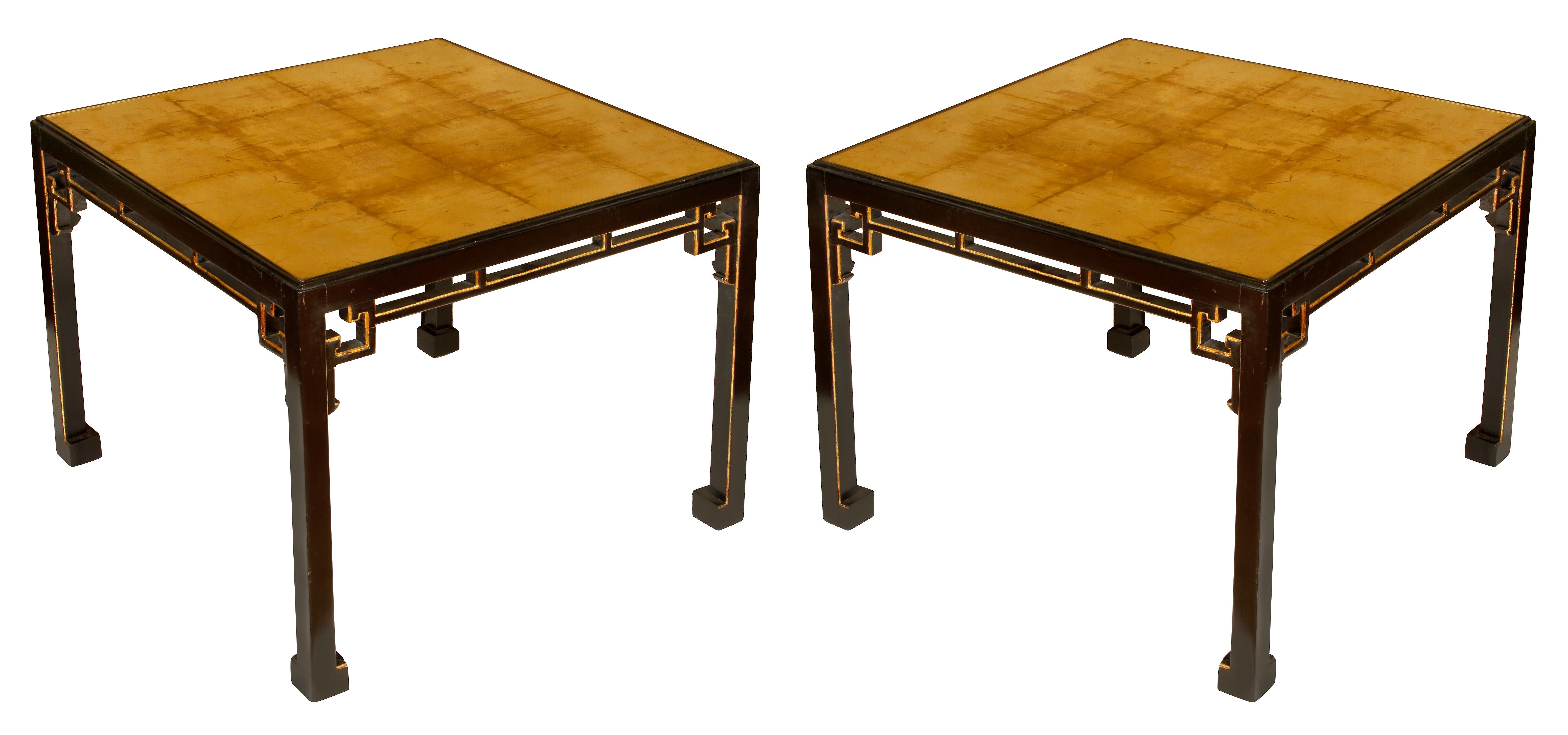 A pair of gilt and antiqued mirror top side tables in the style of James Mont. Black table legs in Chinese inspired shape with gilt detail.