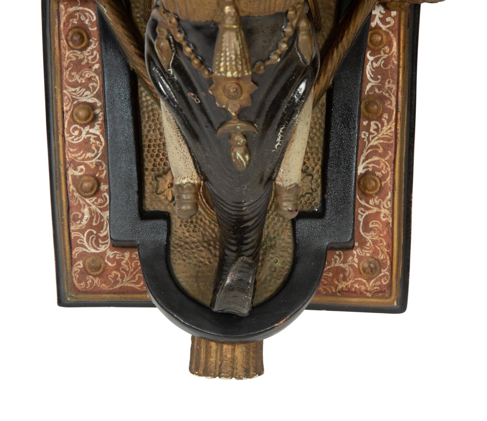 Cette paire d'appliques murales en forme d'éléphant en faïence présente des détails riches et complexes. Chaque support présente une tête d'éléphant sculptée, ornée de dorures et de peintures élaborées, reflétant la grandeur des influences exotiques